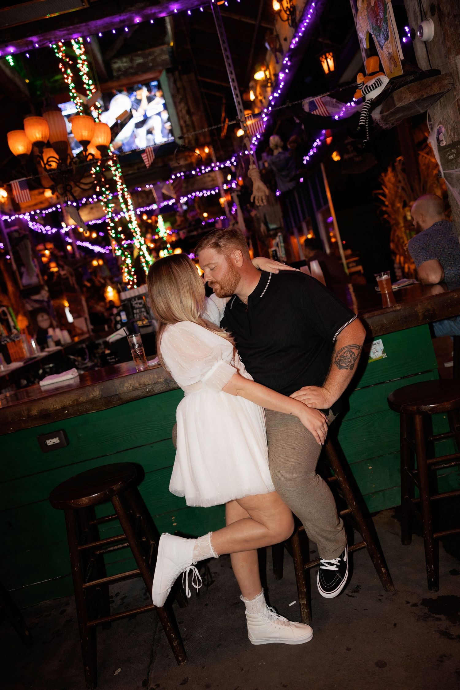A romantic dance moment in a bar decorated with colorful lights and festive decorations.