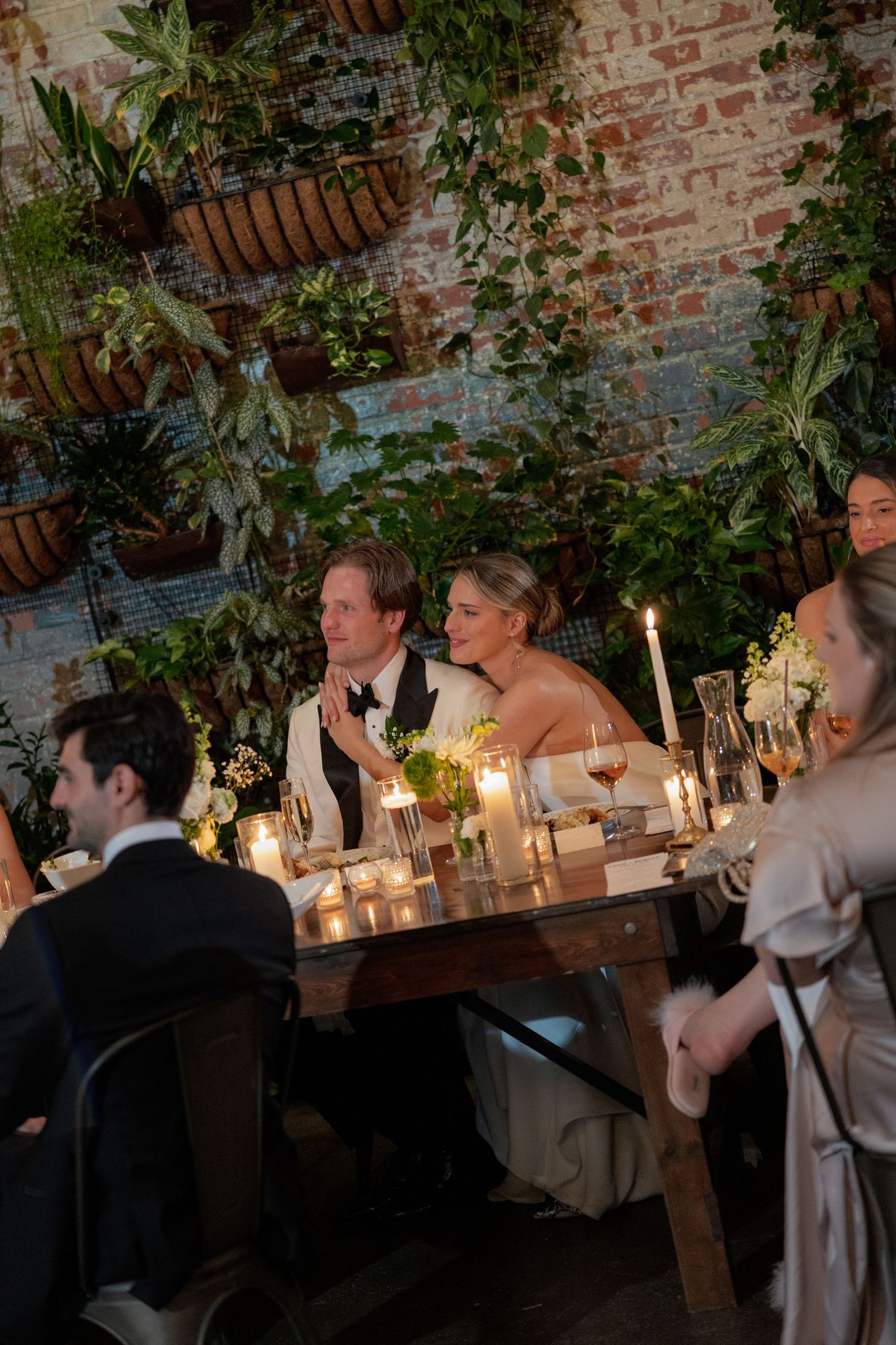 Candlelit wedding dinner table with exposed brick walls and greenery decorations creating an intimate atmosphere.
