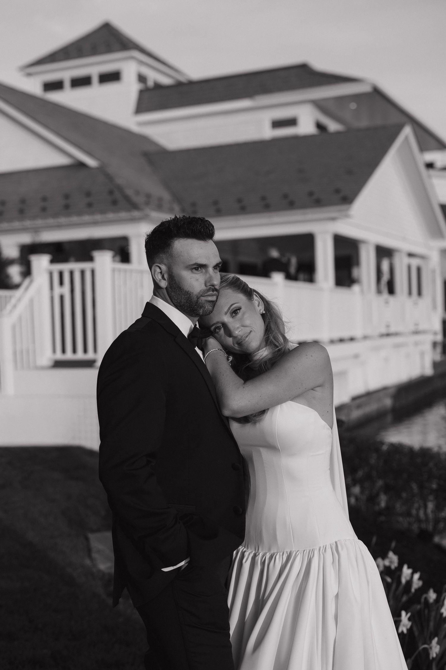 Black and white wedding photo of bride and groom embracing outside elegant white venue.