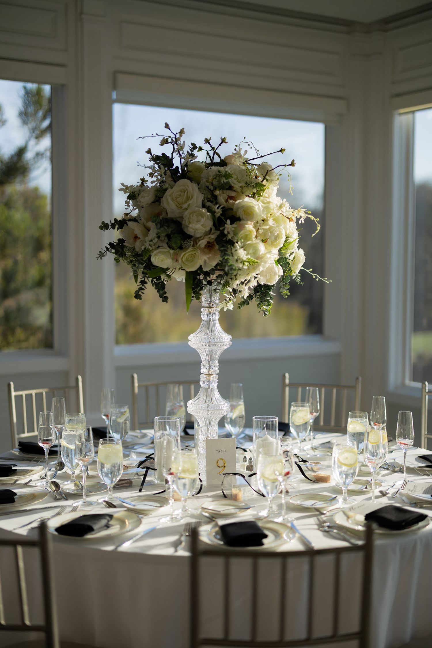 Tall crystal vase with lush white floral centerpiece on an elegantly set wedding reception table.