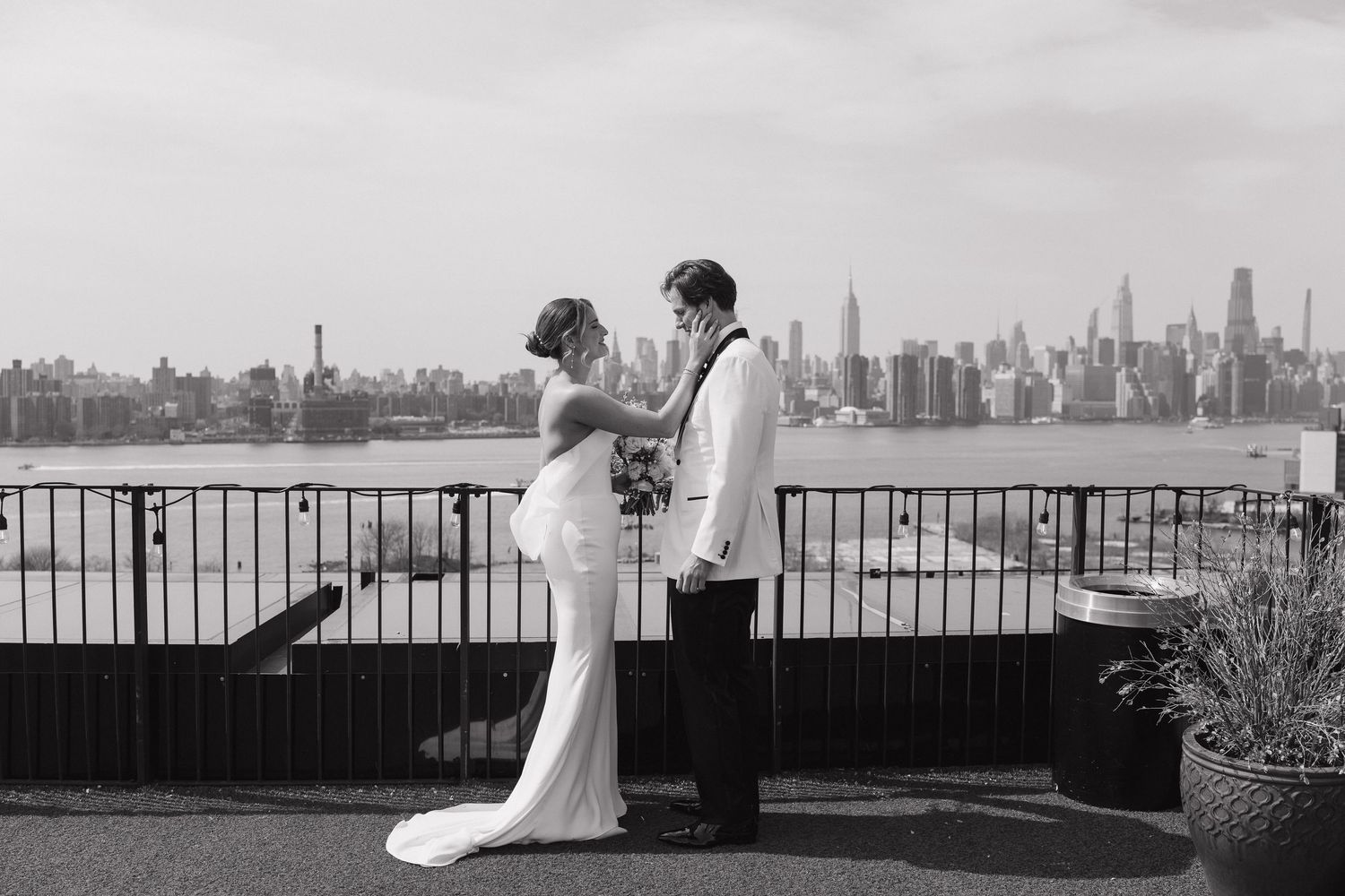 Black and white photo of a wedding couple embracing on a rooftop terrace with New York City skyline in background.