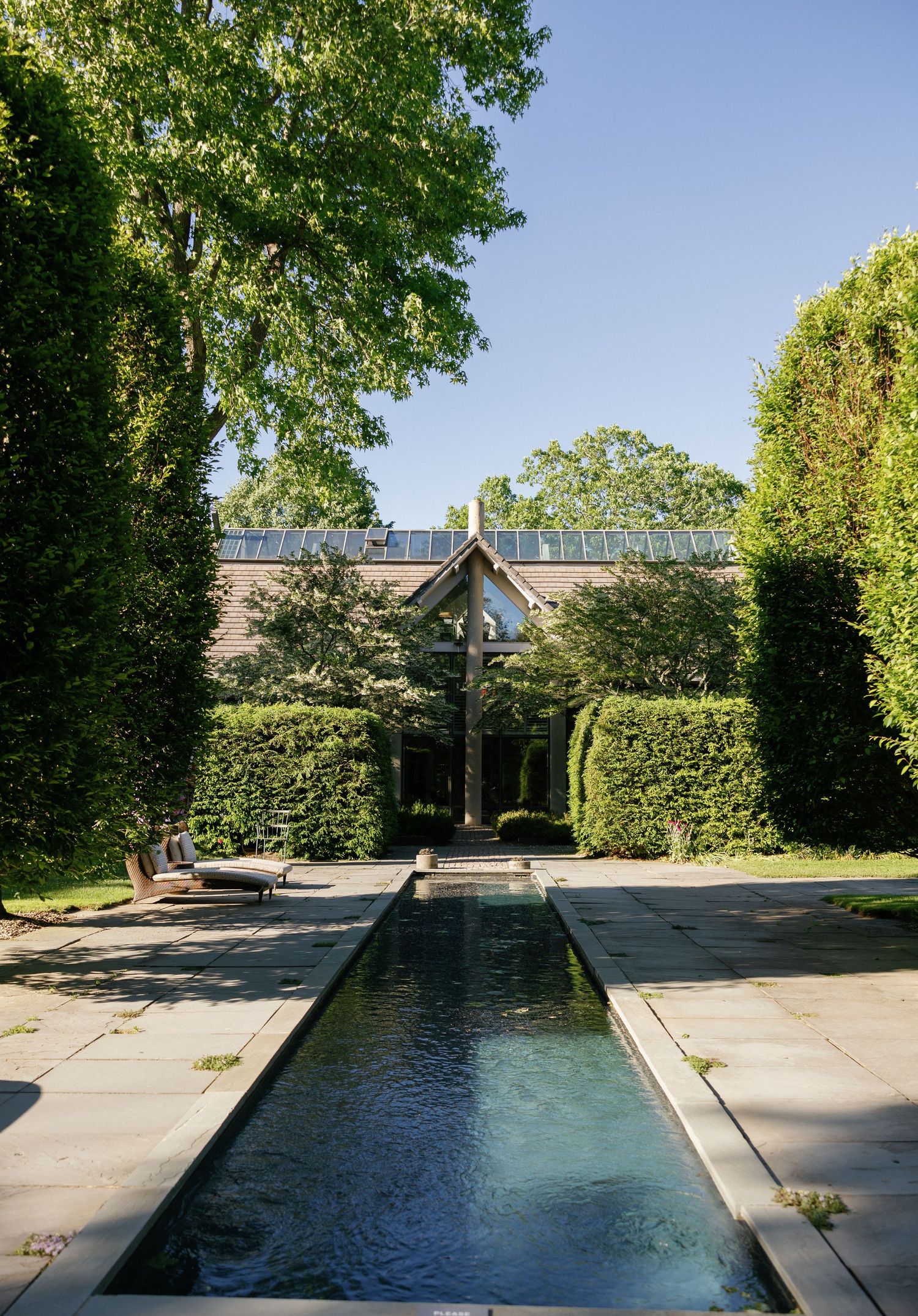 Long rectangular reflecting pool surrounded by manicured hedges and trees in a formal garden setting.