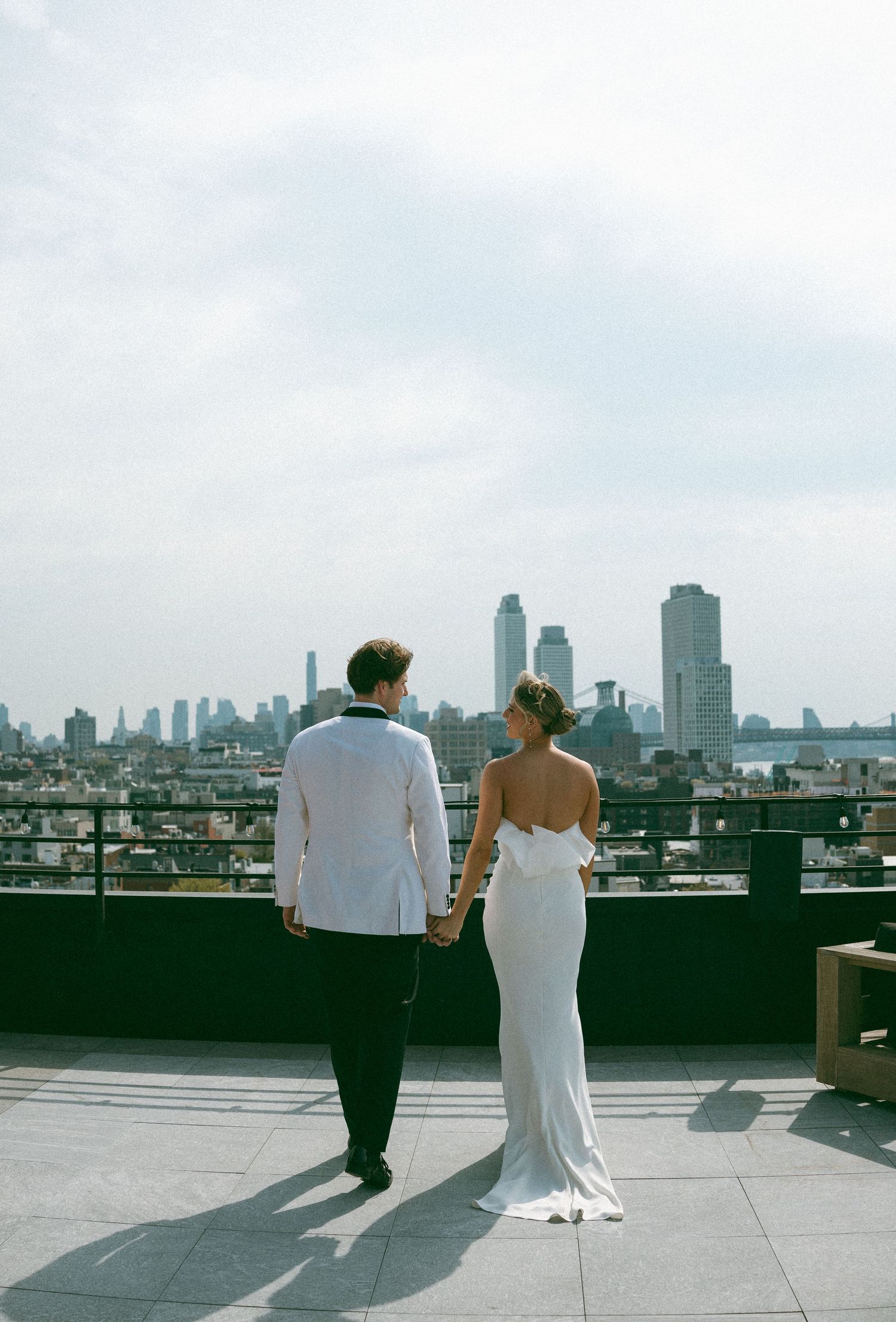 A couple admires the New York City skyline from a rooftop terrace on their wedding day.