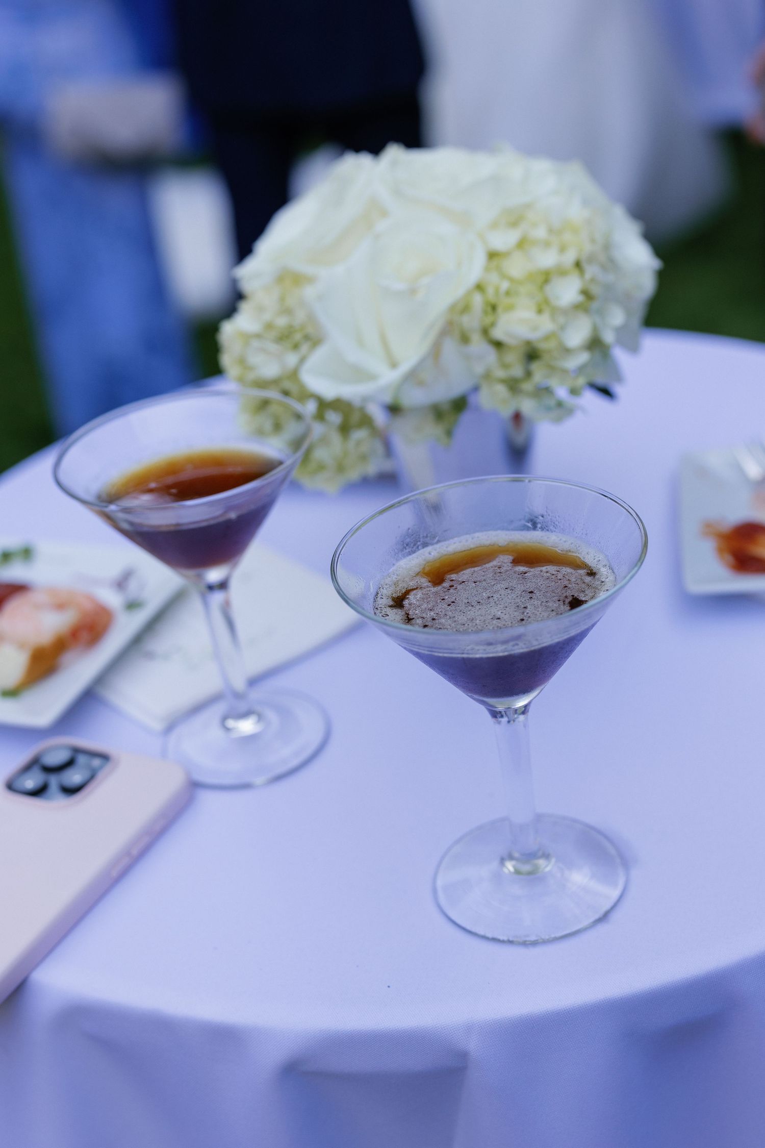 Elegant cocktails and white hydrangea flowers arranged on a white tablecloth at a wedding reception.