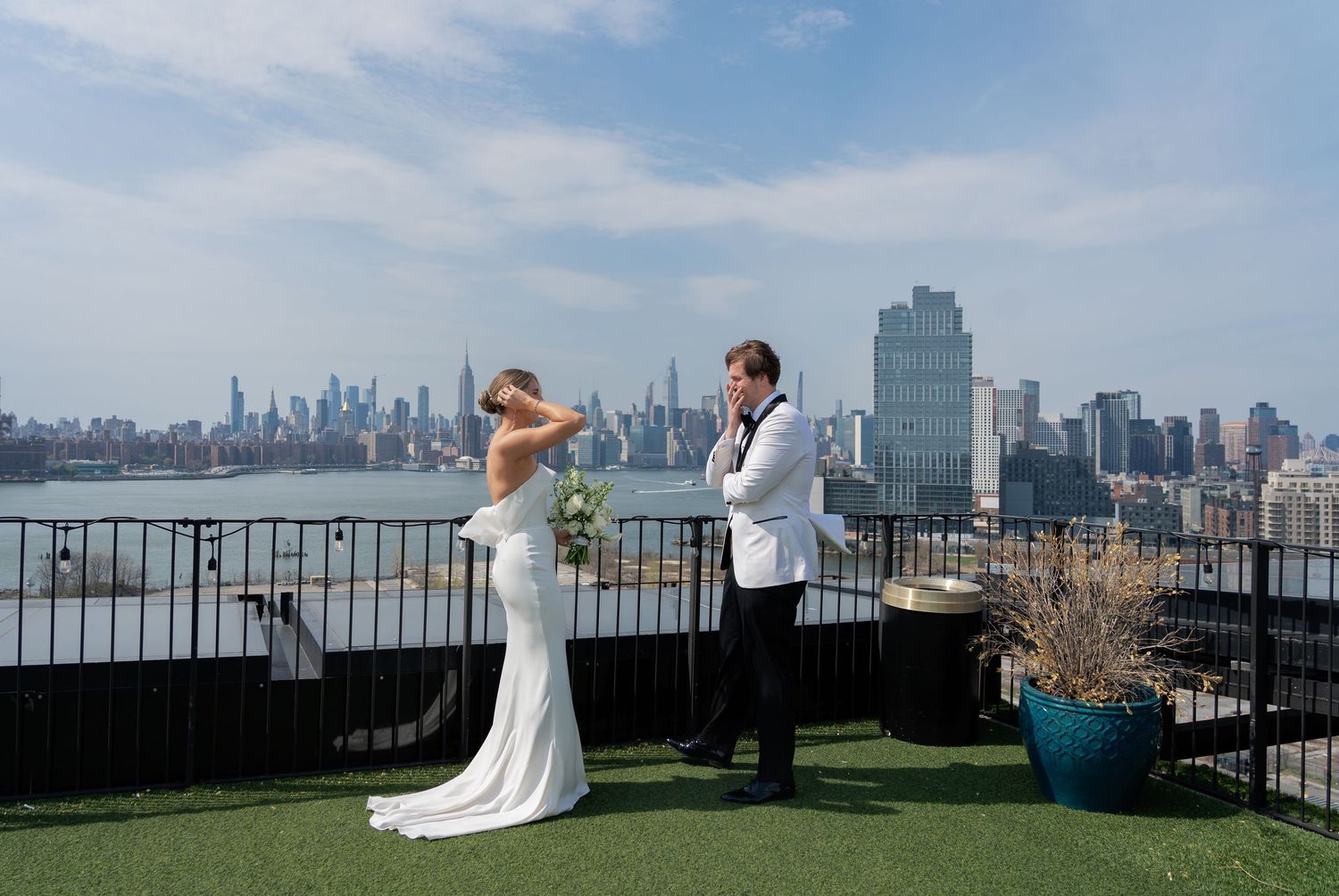 A couple celebrates their wedding day on a rooftop terrace overlooking the Manhattan skyline on a sunny day.