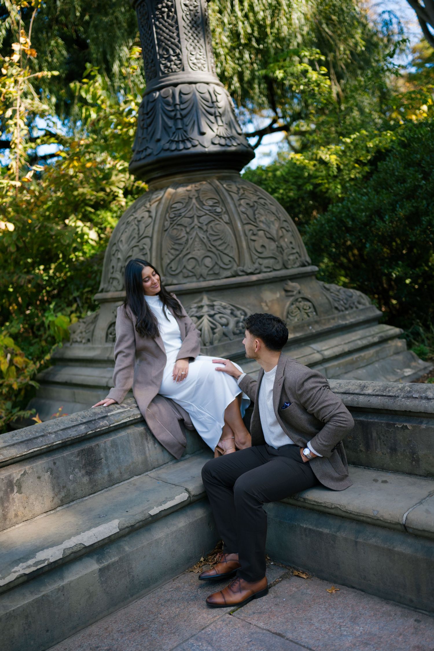 Couple sitting on ornate stone steps in a garden setting with fall foliage in the background.