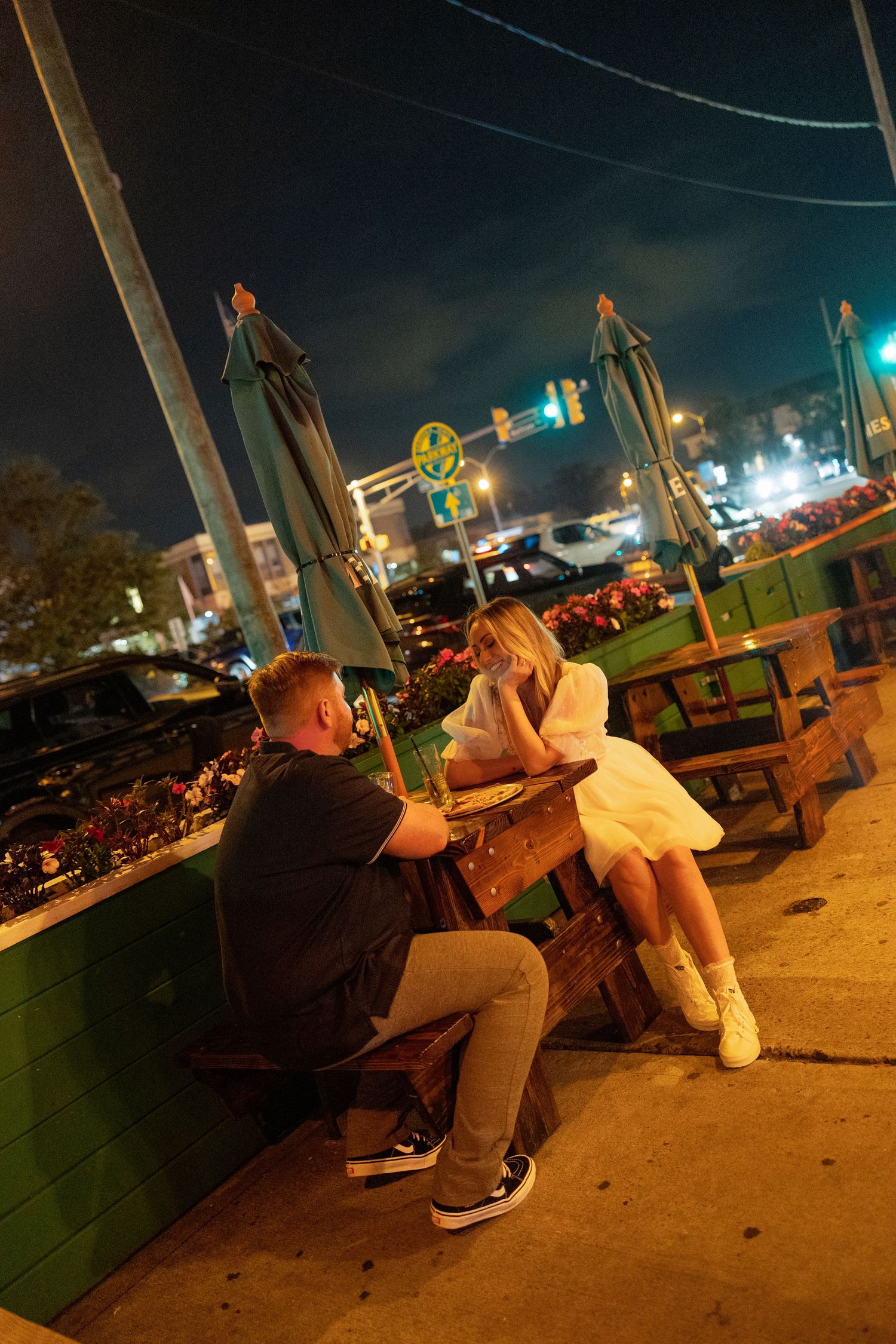 People sitting on benches at night with colorful string lights illuminating the outdoor space.