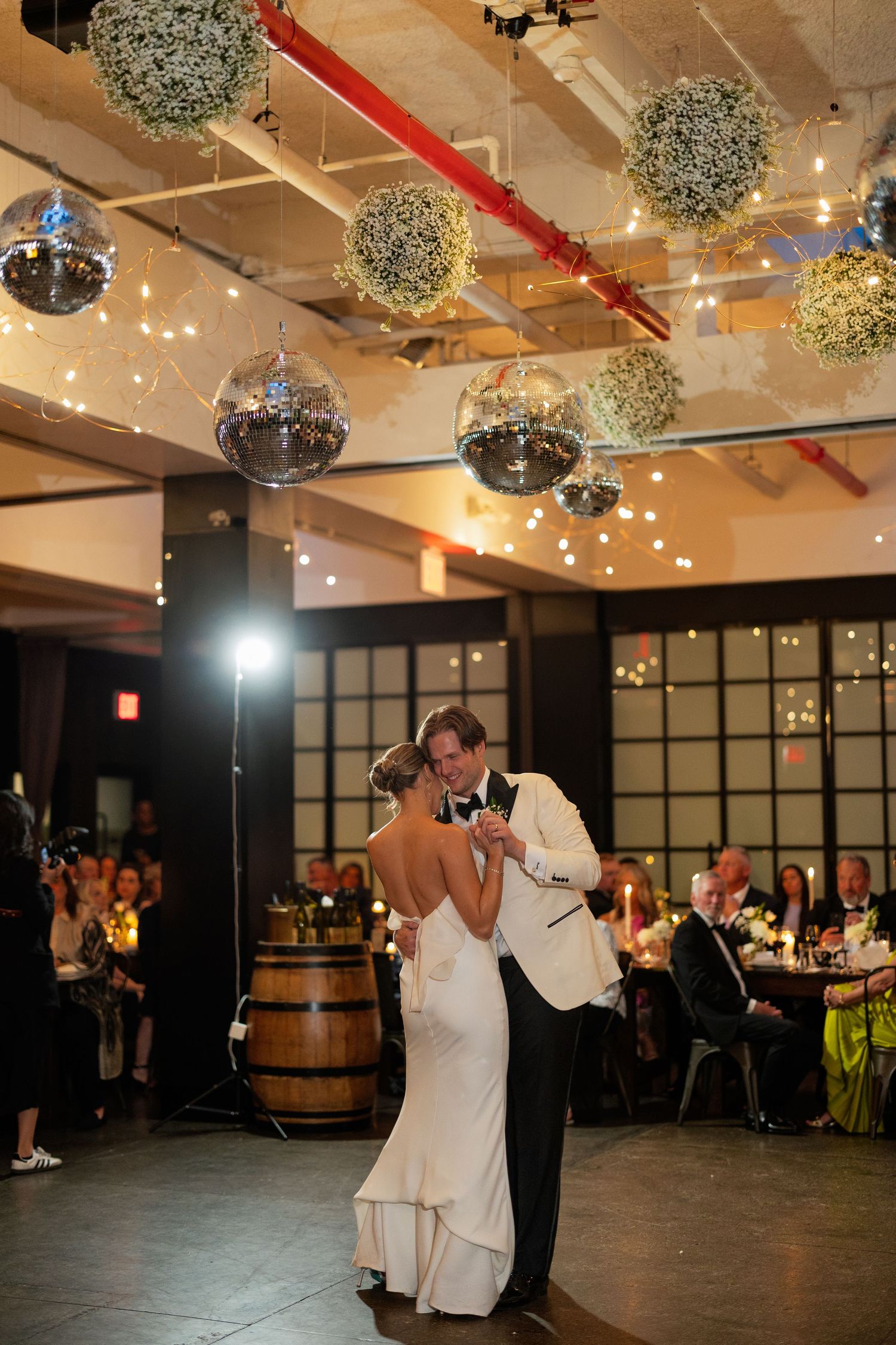 Wedding reception dance floor in an industrial venue with hanging baby's breath balls and string lights.