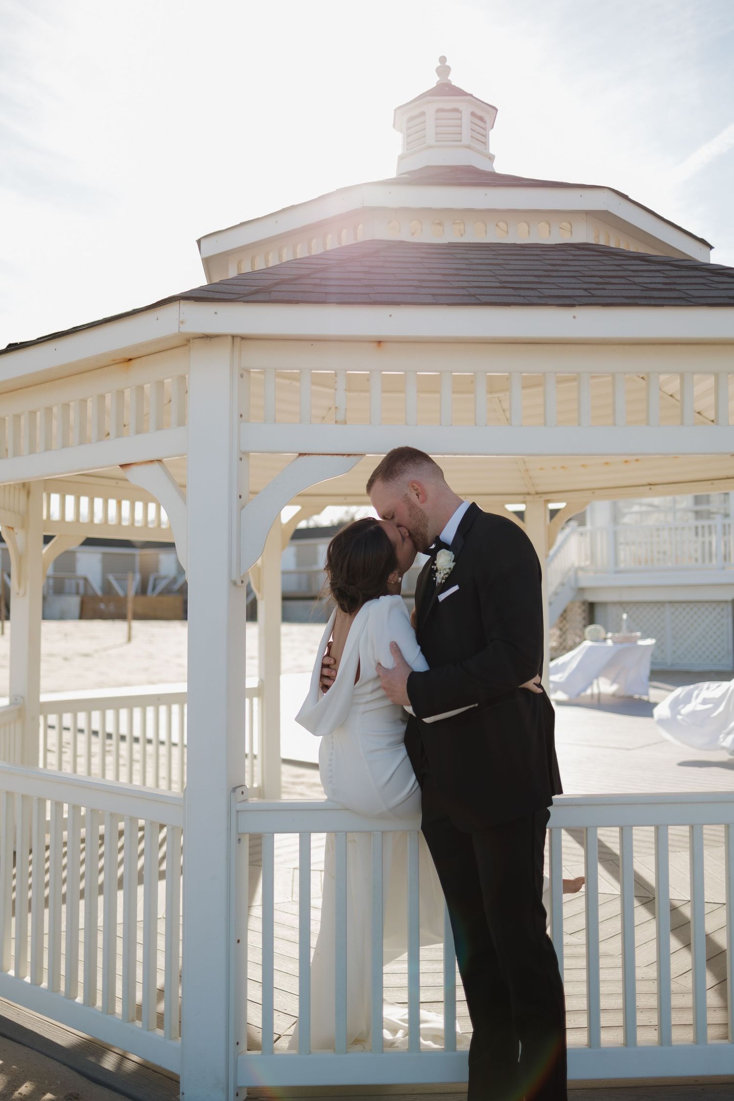 A romantic moment captured in a white gazebo as a couple shares a kiss during their wedding ceremony.
