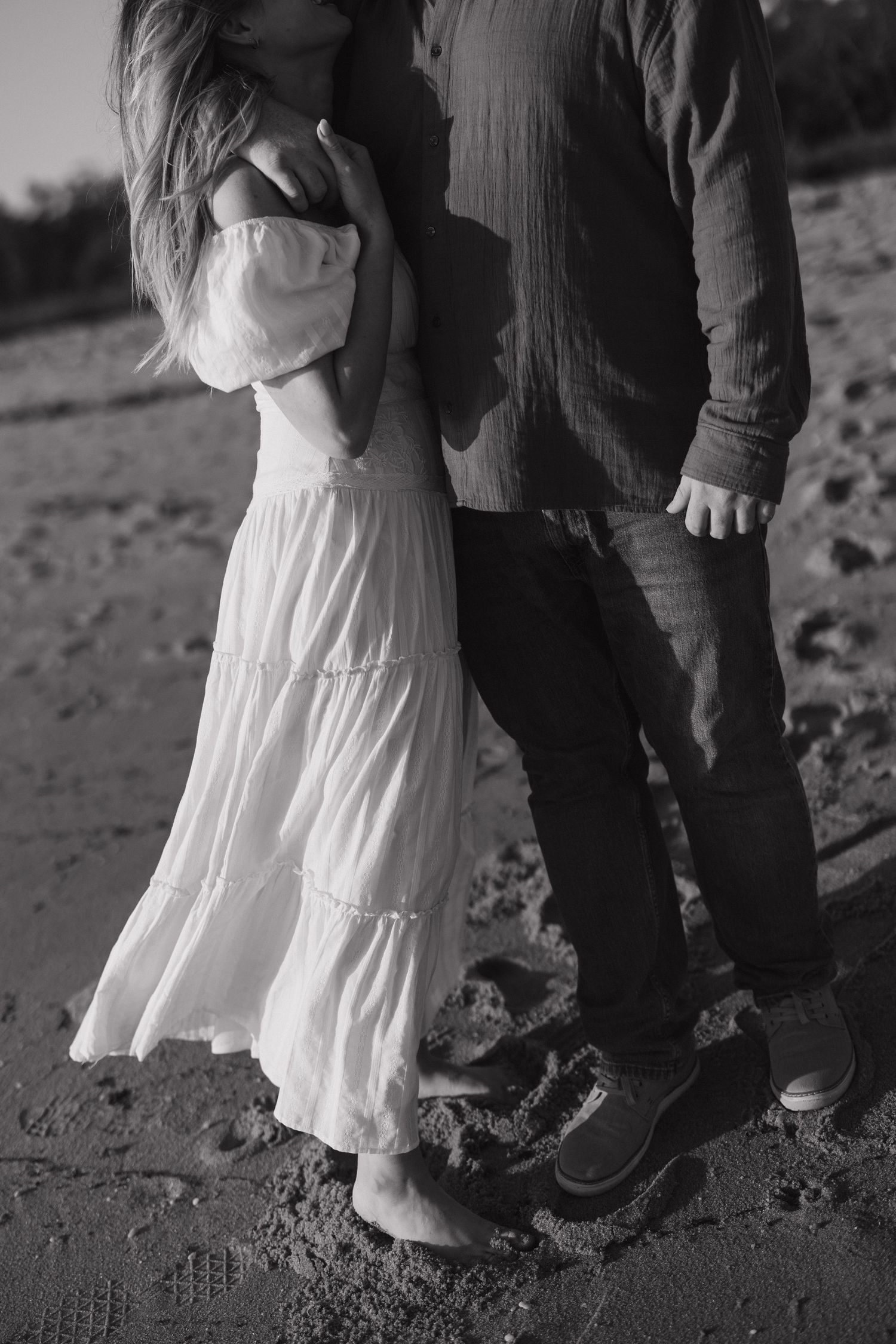 Black and white photo showing details of a flowing white dress and casual attire on a beach.