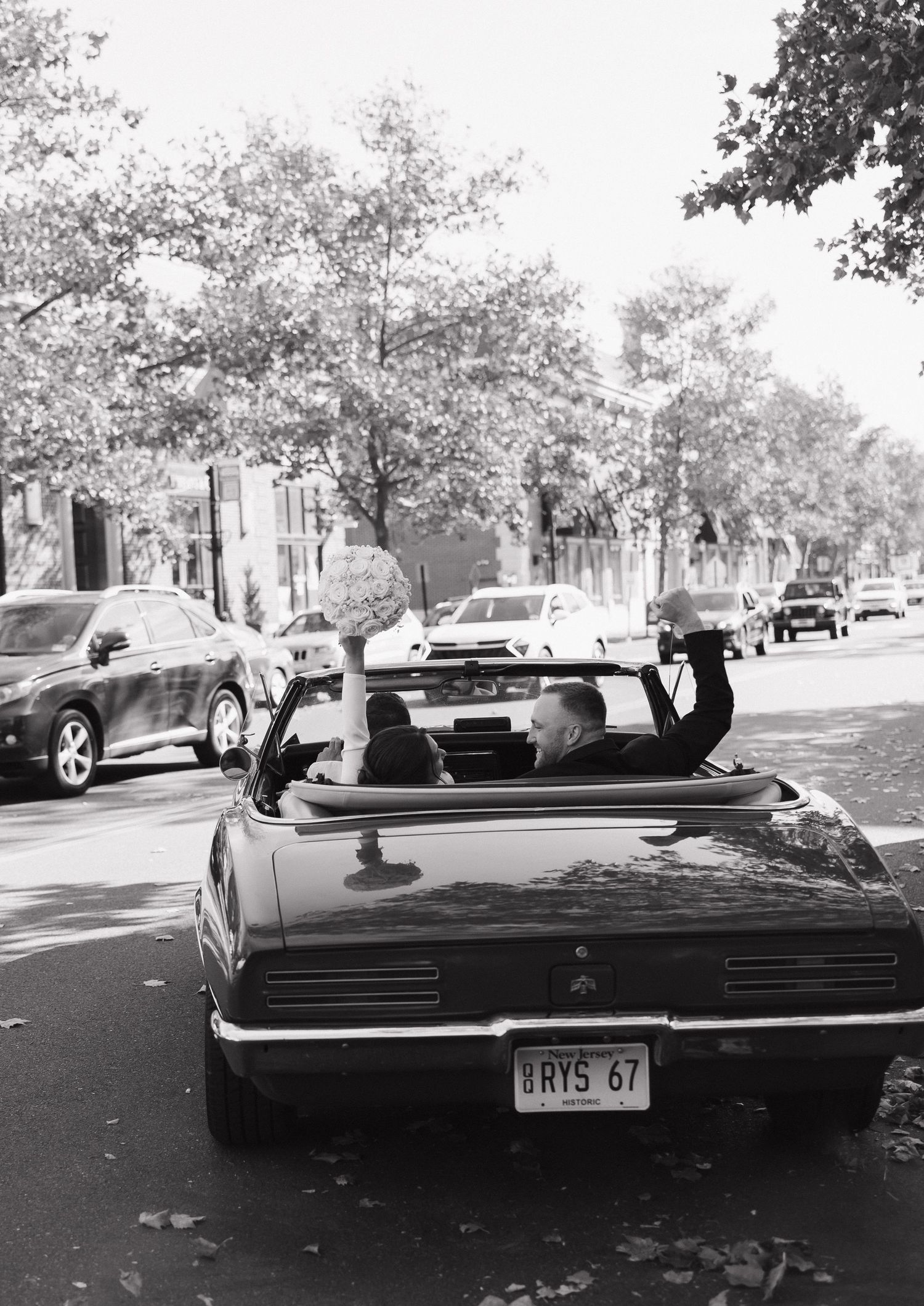 Vintage black convertible car parked on a tree-lined street in black and white photography.