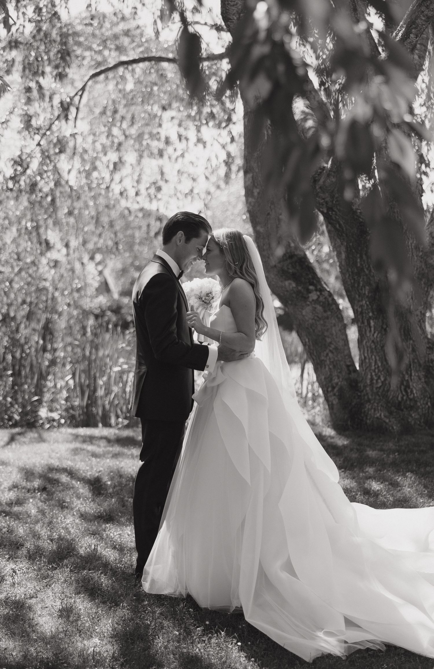 A romantic wedding photoshoot in black and white showing flowing white dress details under garden trees.
