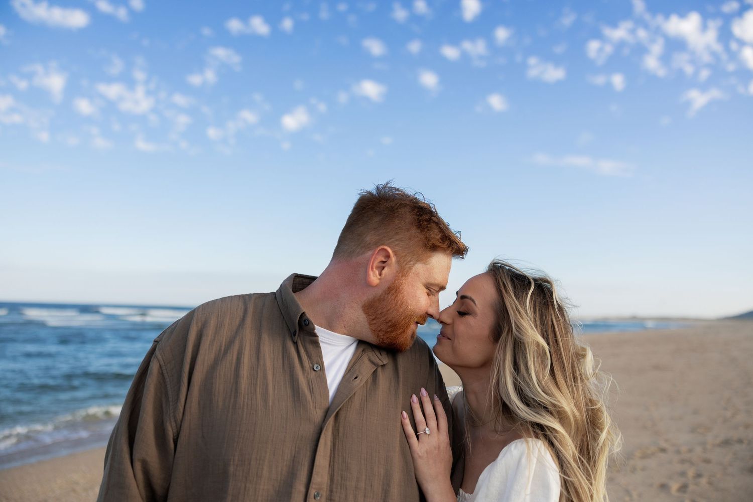 Romantic couple sharing intimate moments together on a sandy beach at sunset with ocean waves in background.