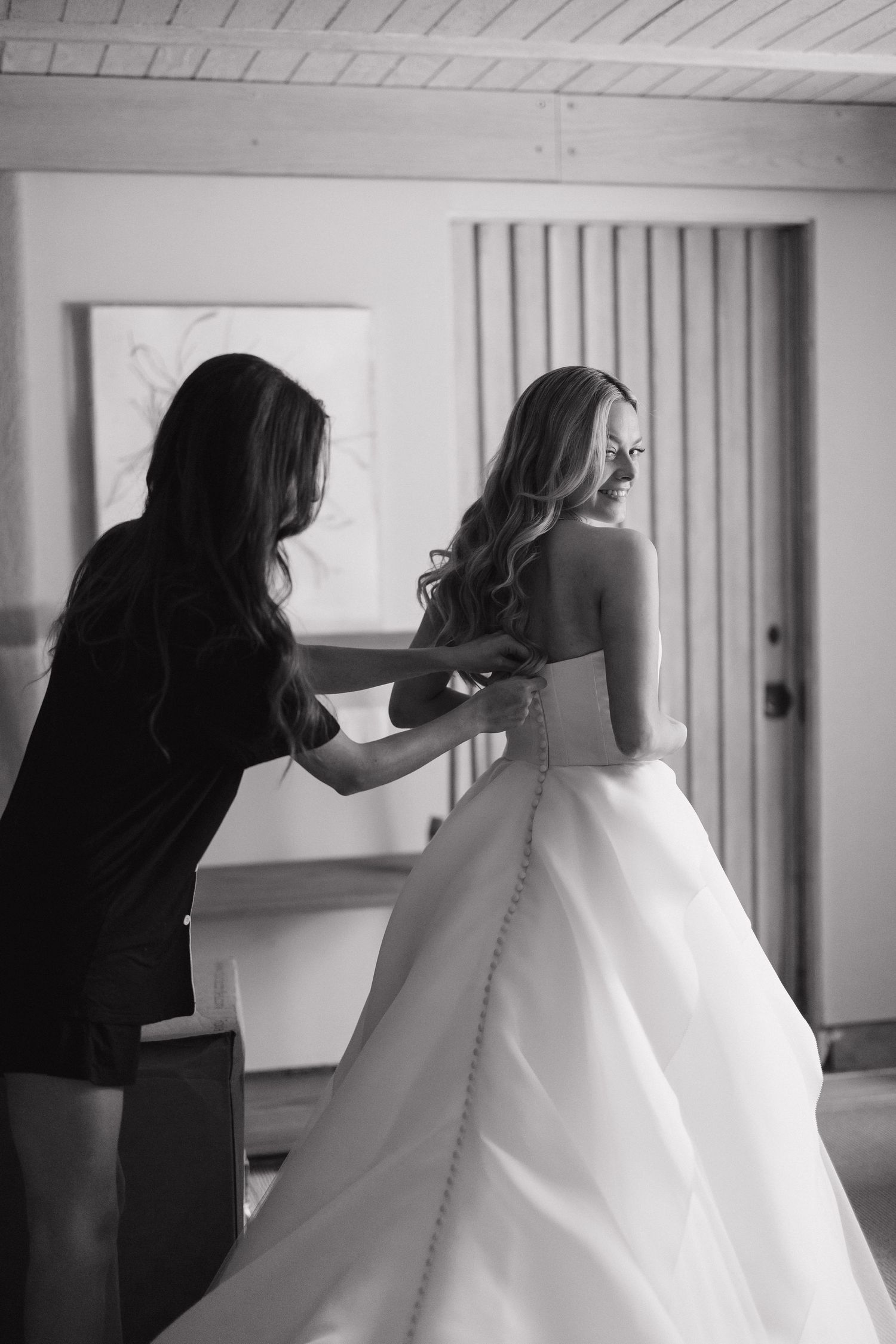 Behind-the-scenes sequence showing wedding dress preparation and button fastening.