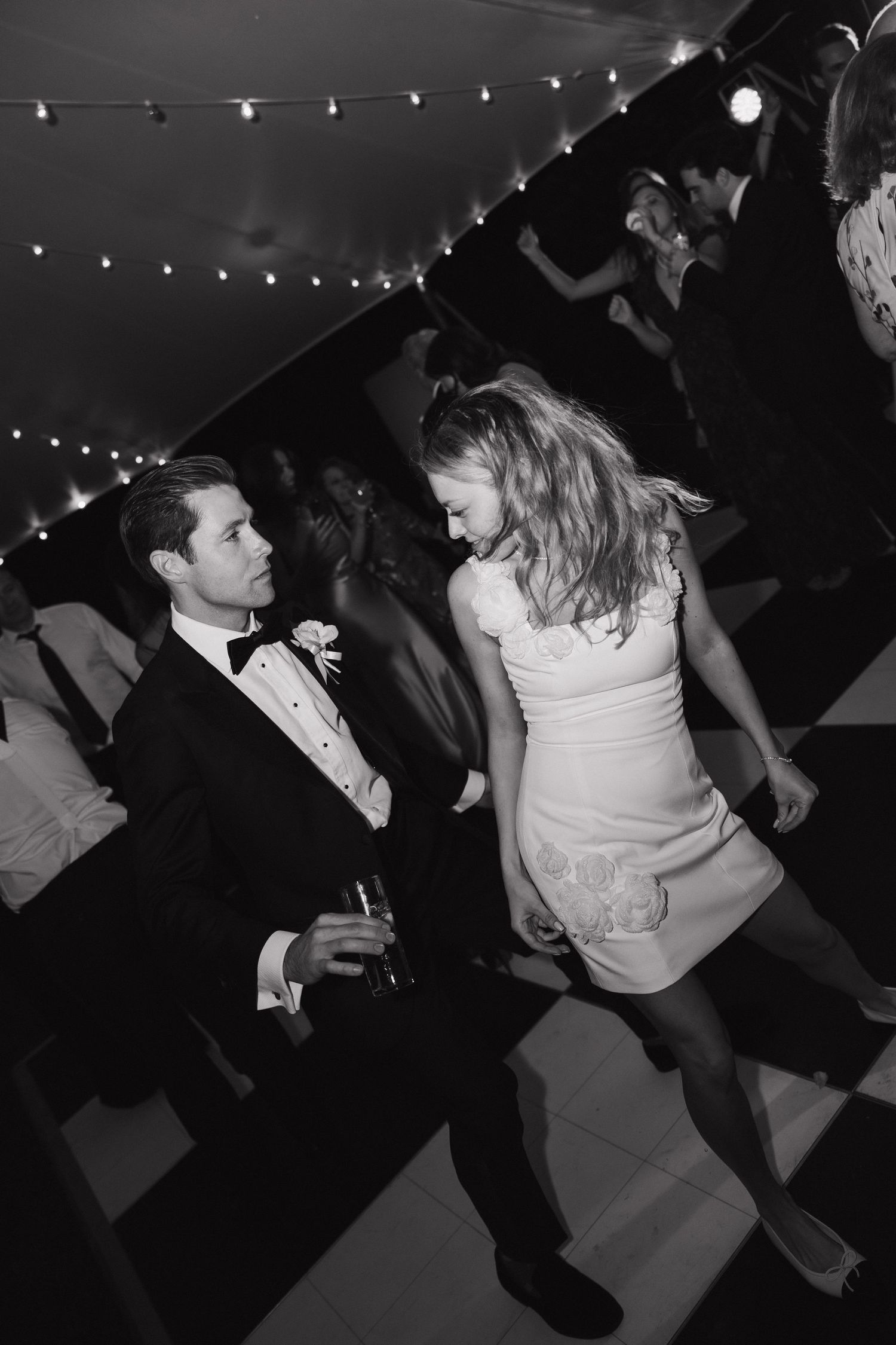 Black and white photos capture dynamic dancing moments under string lights at a wedding reception.