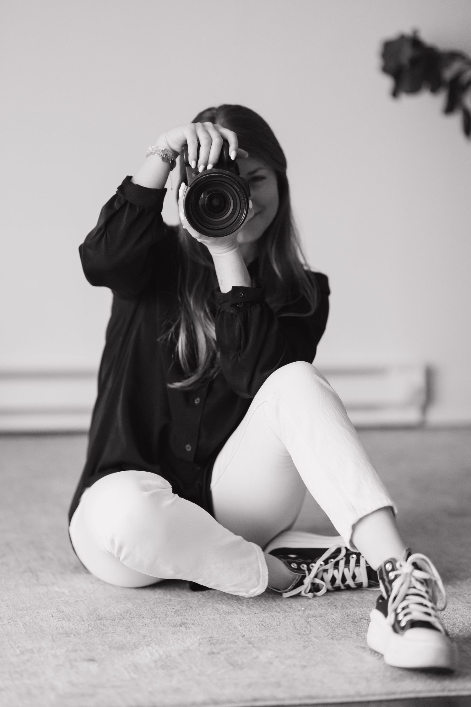 A photographer in casual clothing sits cross-legged while taking a picture.