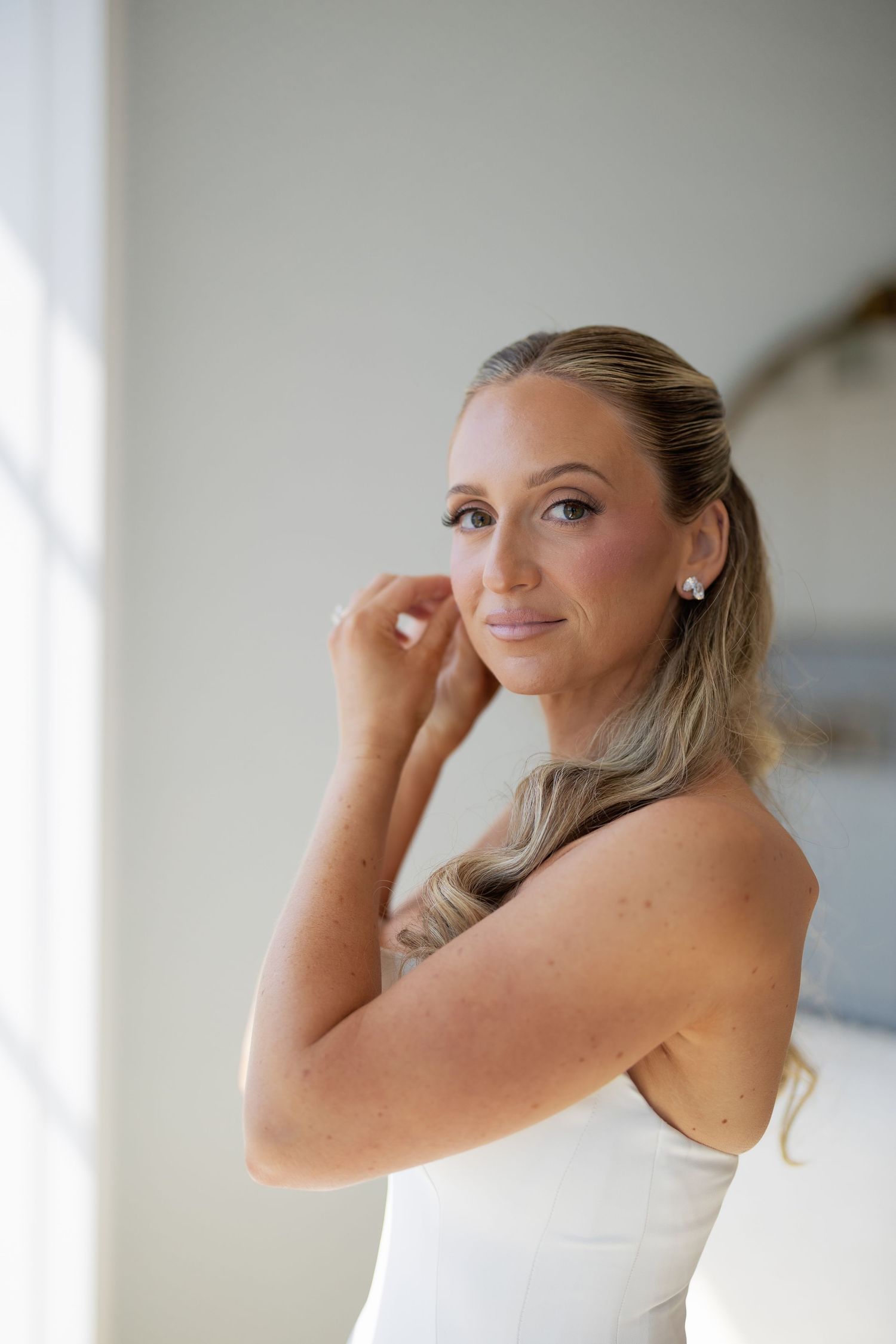 Beautiful bride with natural glowing makeup and elegant low ponytail wearing strapless white wedding gown.