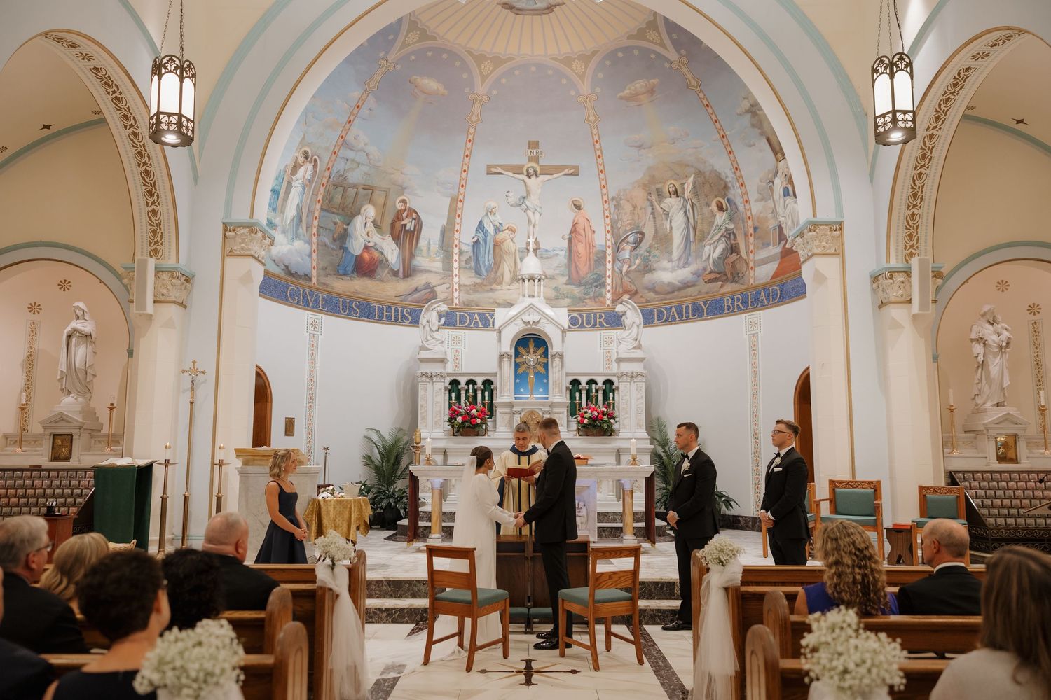 Interior panoramic view of a traditional Catholic church sanctuary with ornate murals, arches, and altar decorations.