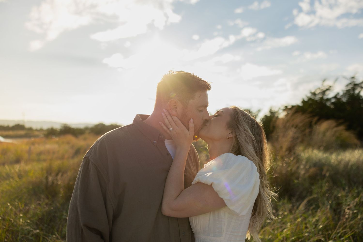 Couple sharing tender moments in golden sunlight against a rural landscape.