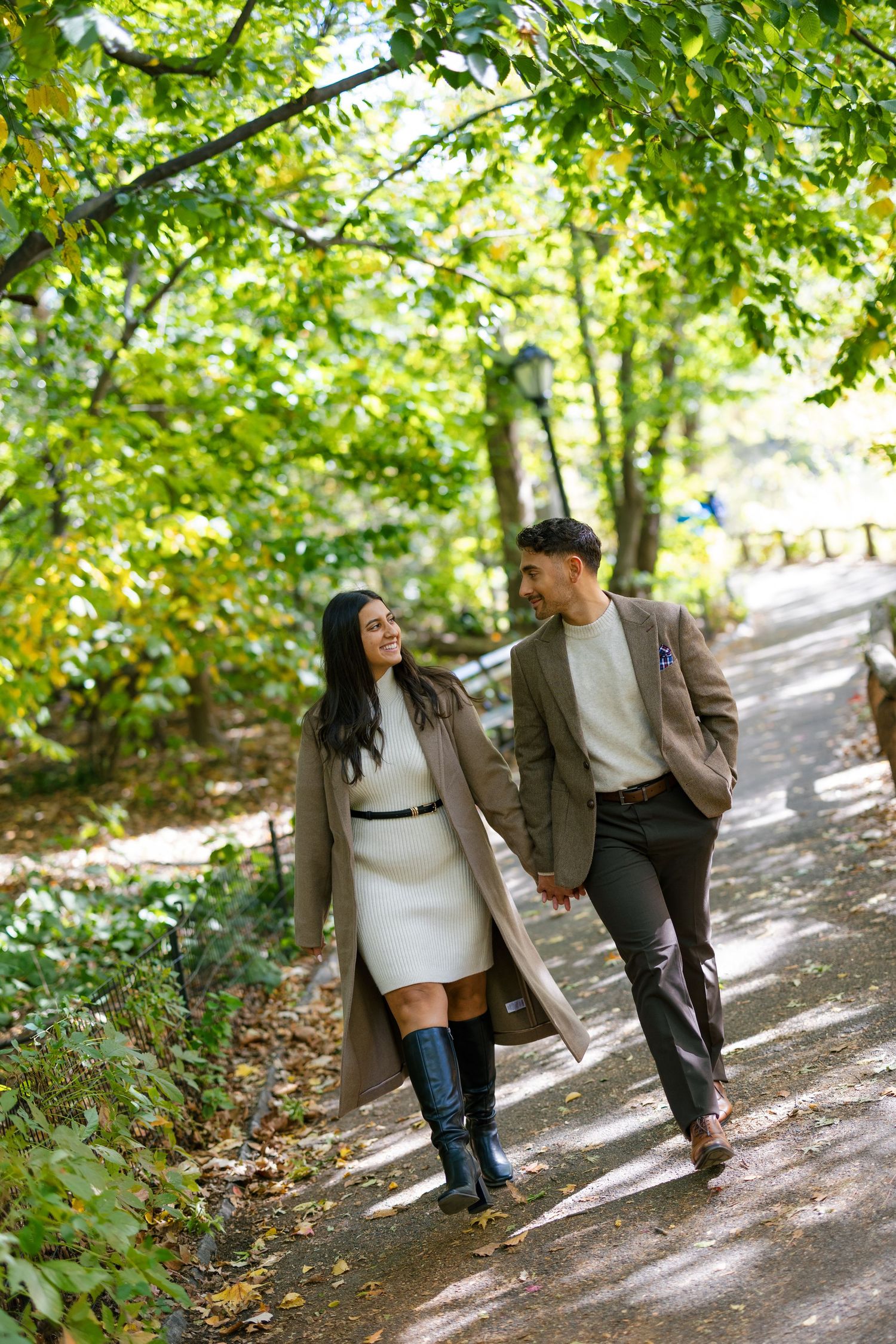 Couple walking together on a sunlit autumn path through trees.