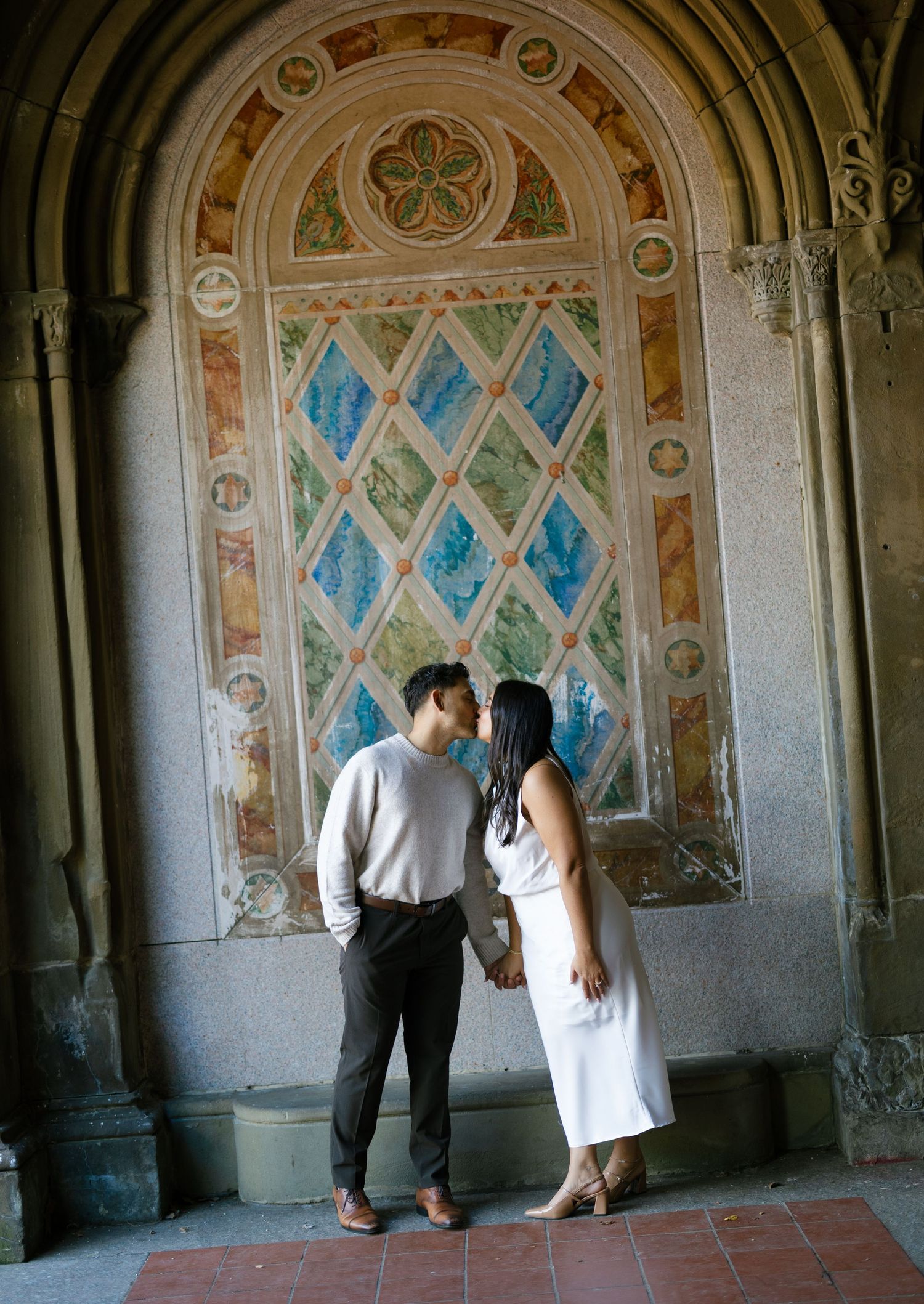 A couple poses together against an ornate archway with decorative blue stained glass patterns.