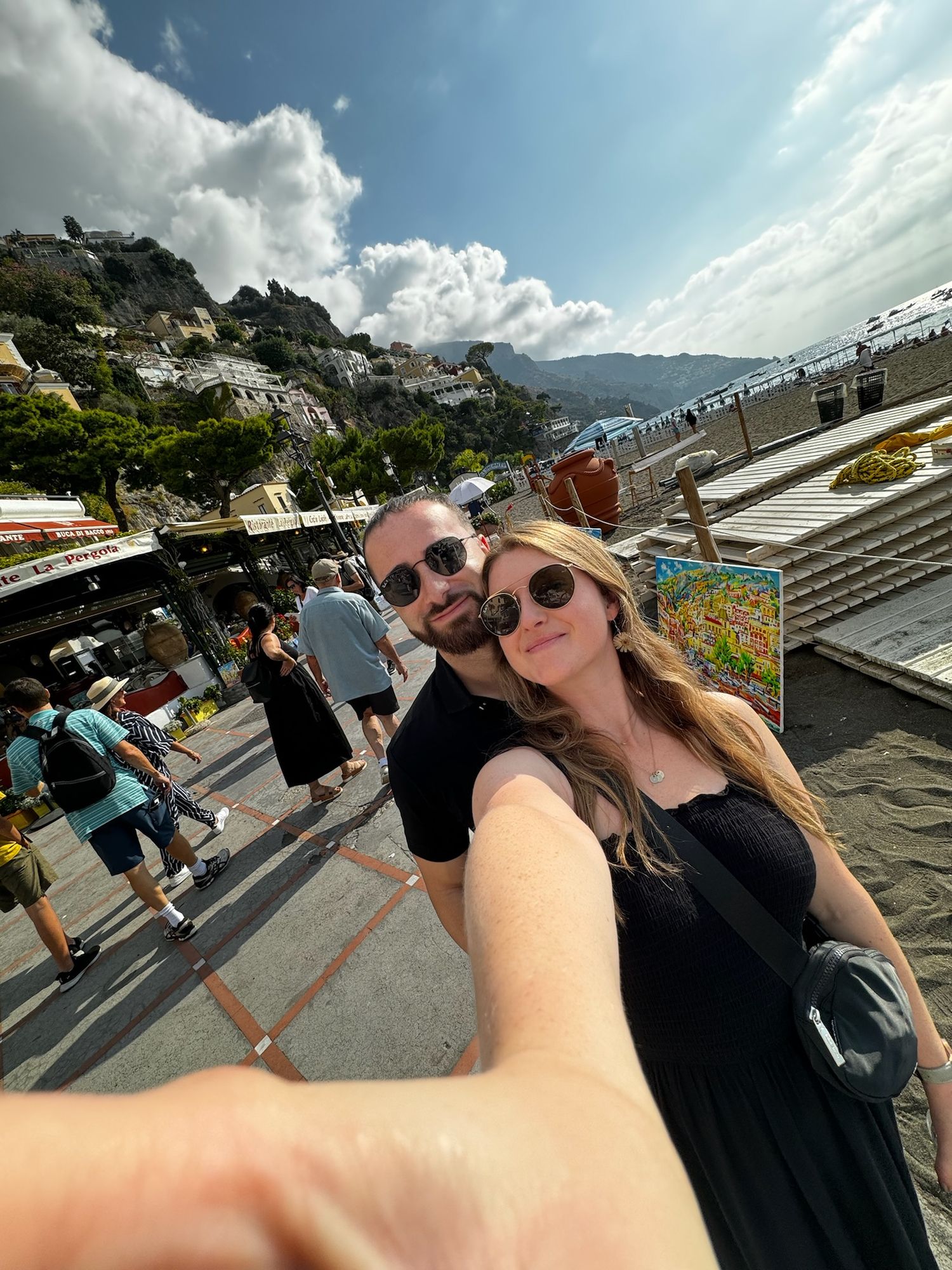 A sunny selfie taken on a crowded hillside street with mountain views.