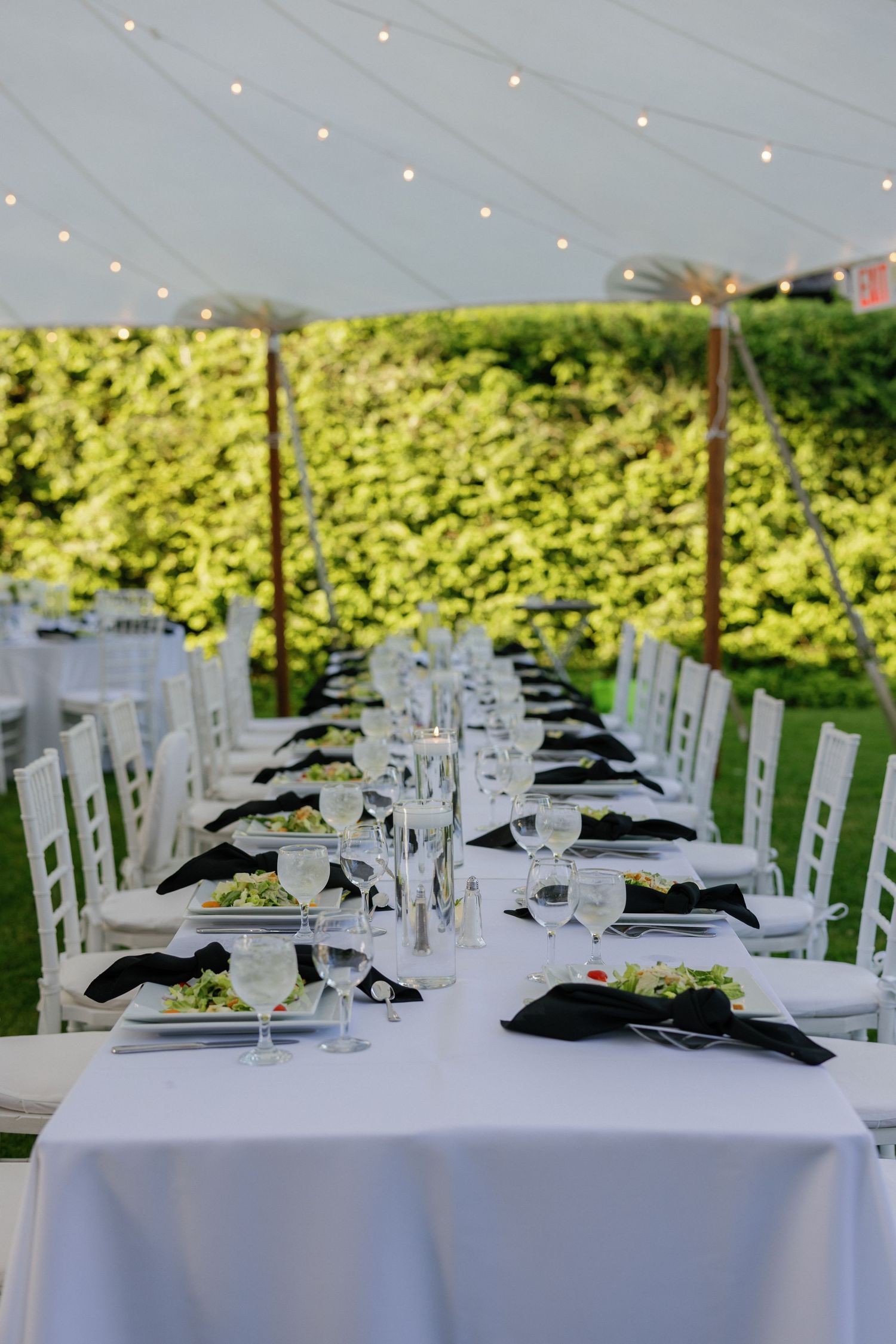 Elegant outdoor wedding reception table settings with white linens and string lights overhead.