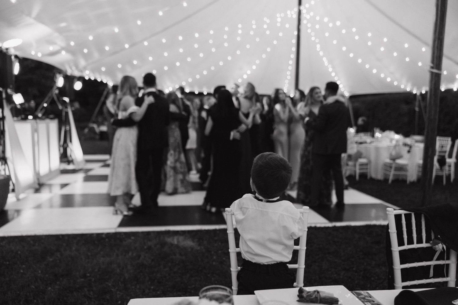 String lights illuminate an outdoor wedding reception tent as guests celebrate on the dance floor.