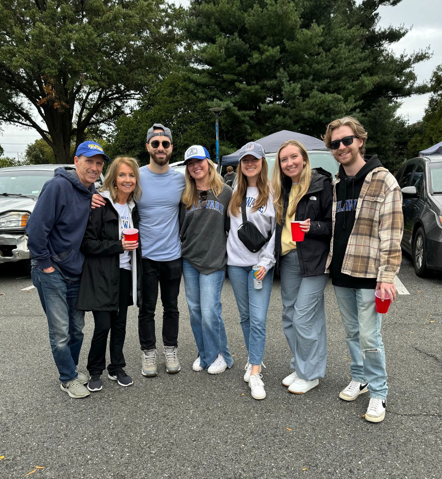 A group of friends pose together outdoors wearing casual attire and sunglasses.