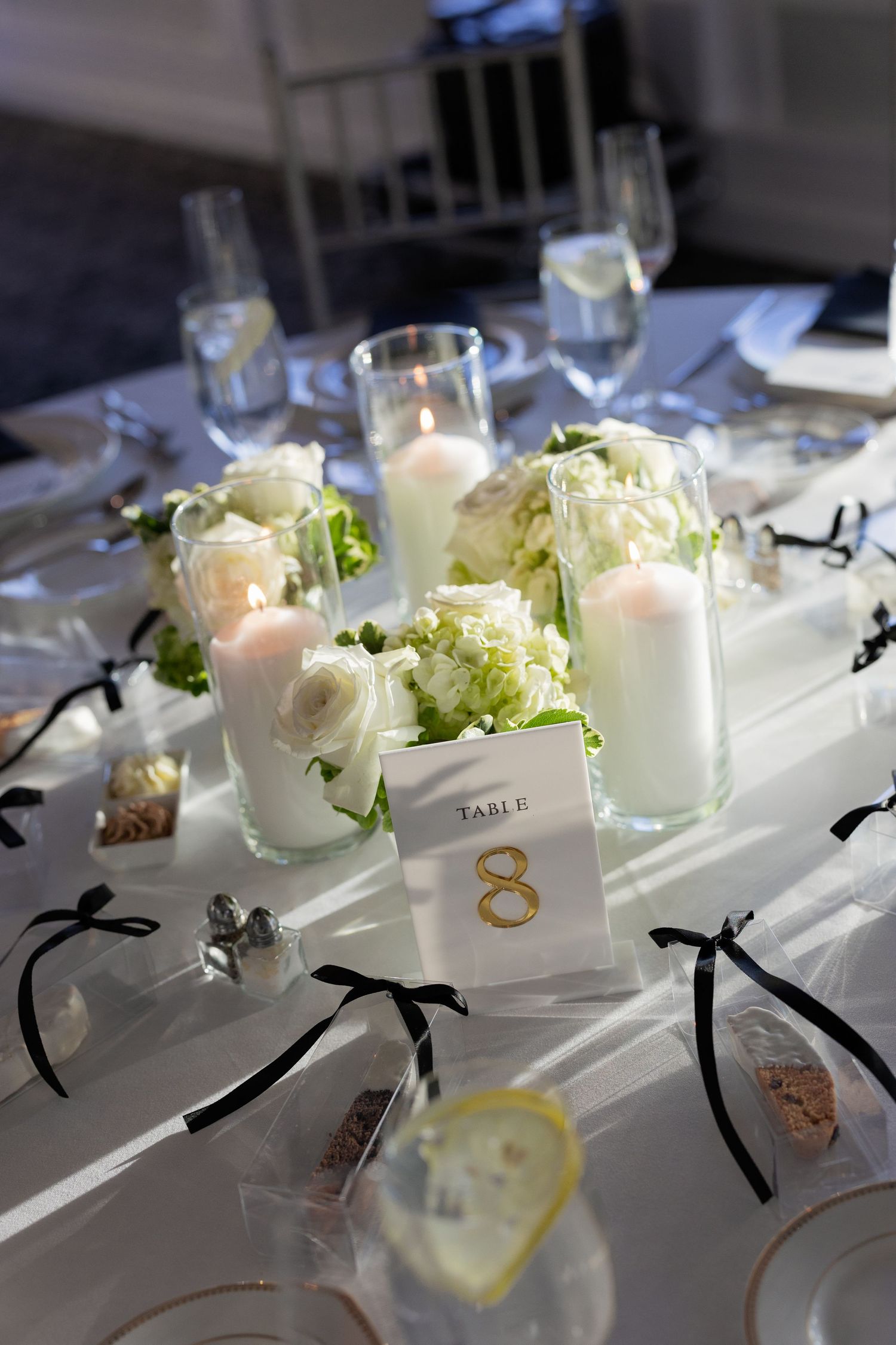 Elegant wedding table setting with white floral centerpieces, pillar candles, and a gold table number 8 card.