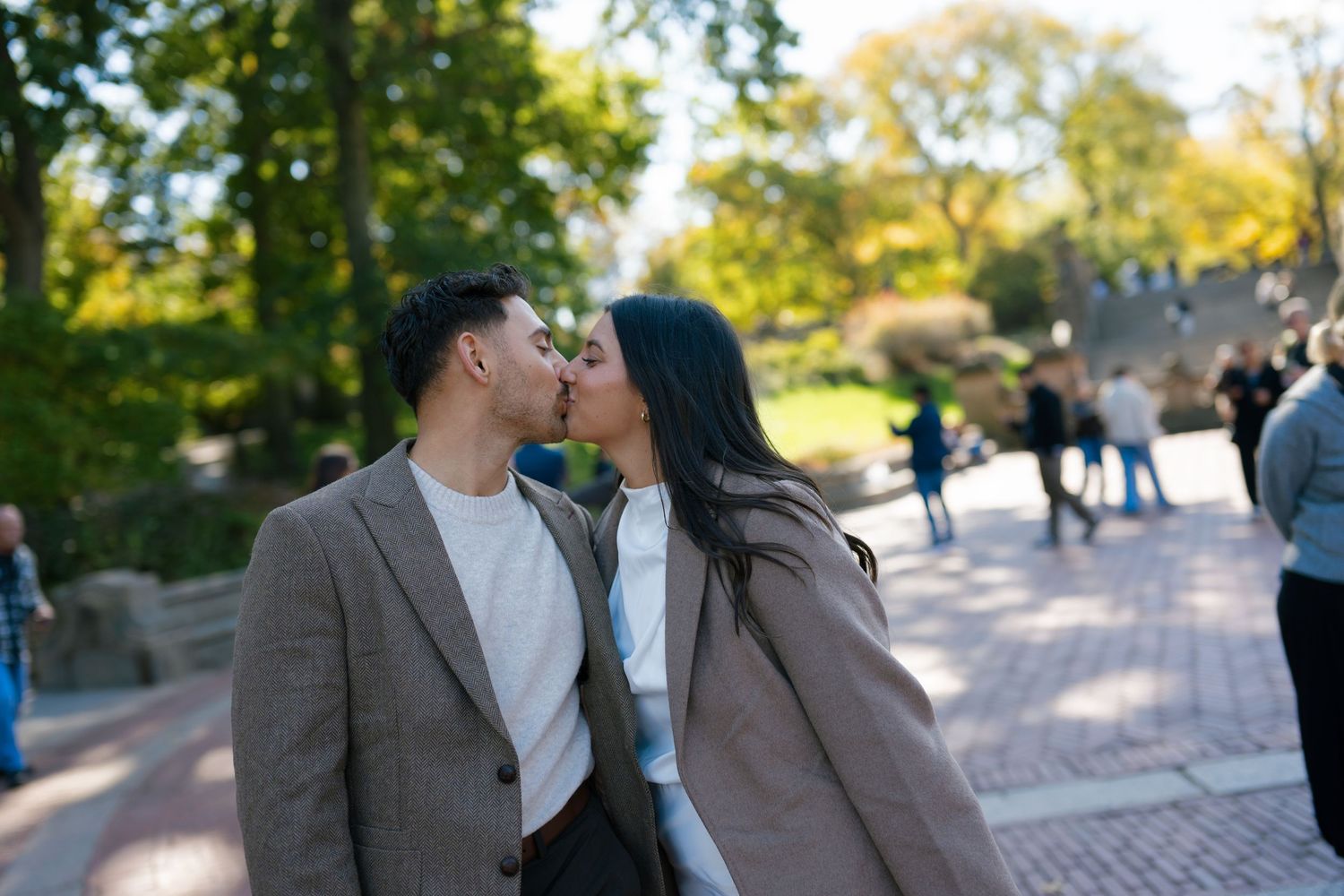 A couple sharing a romantic kiss on a brick path in Central Park on a sunny autumn day.
