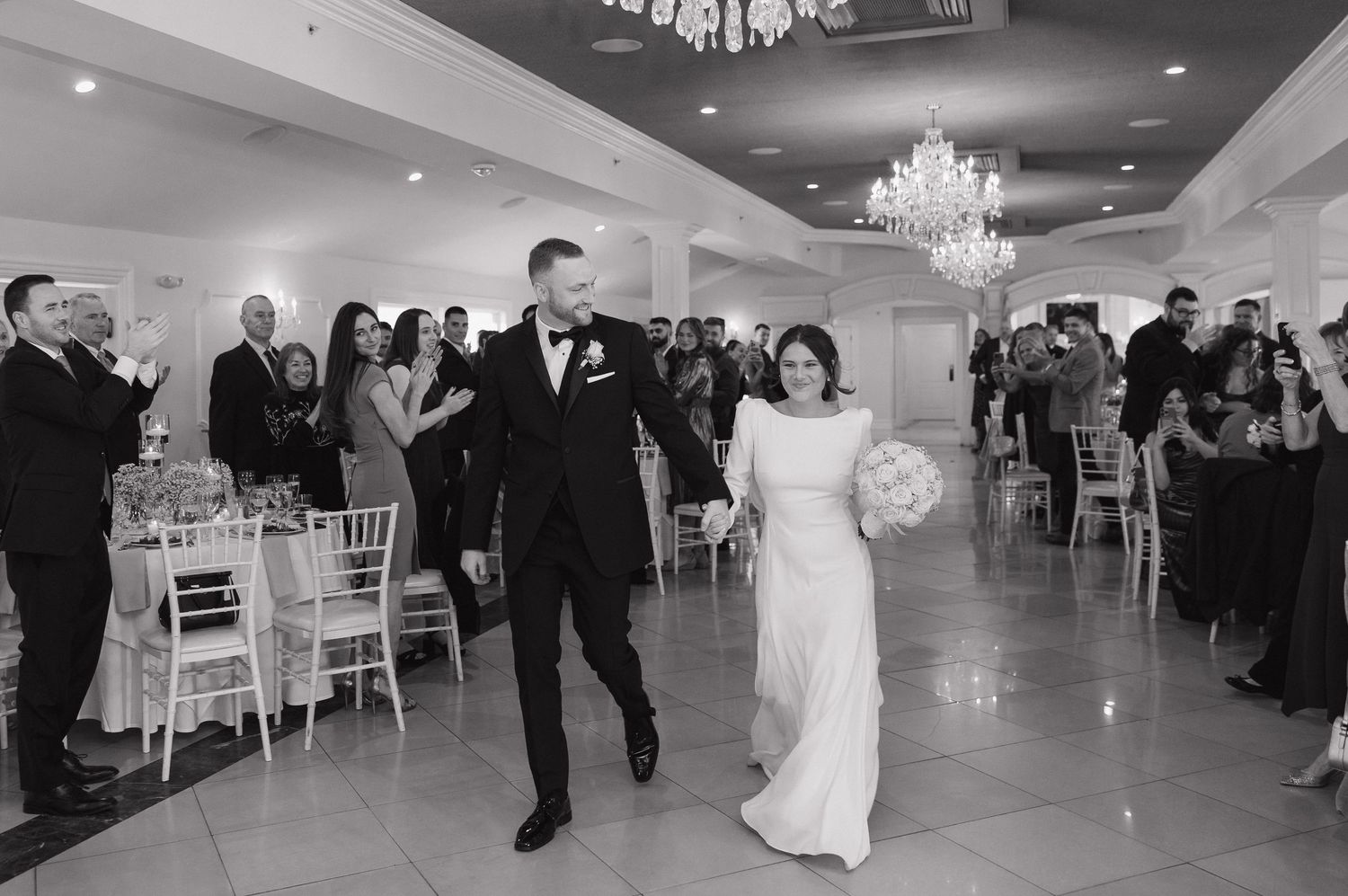 Wedding reception guests dancing on an elegant ballroom floor under crystal chandeliers and soft lighting.