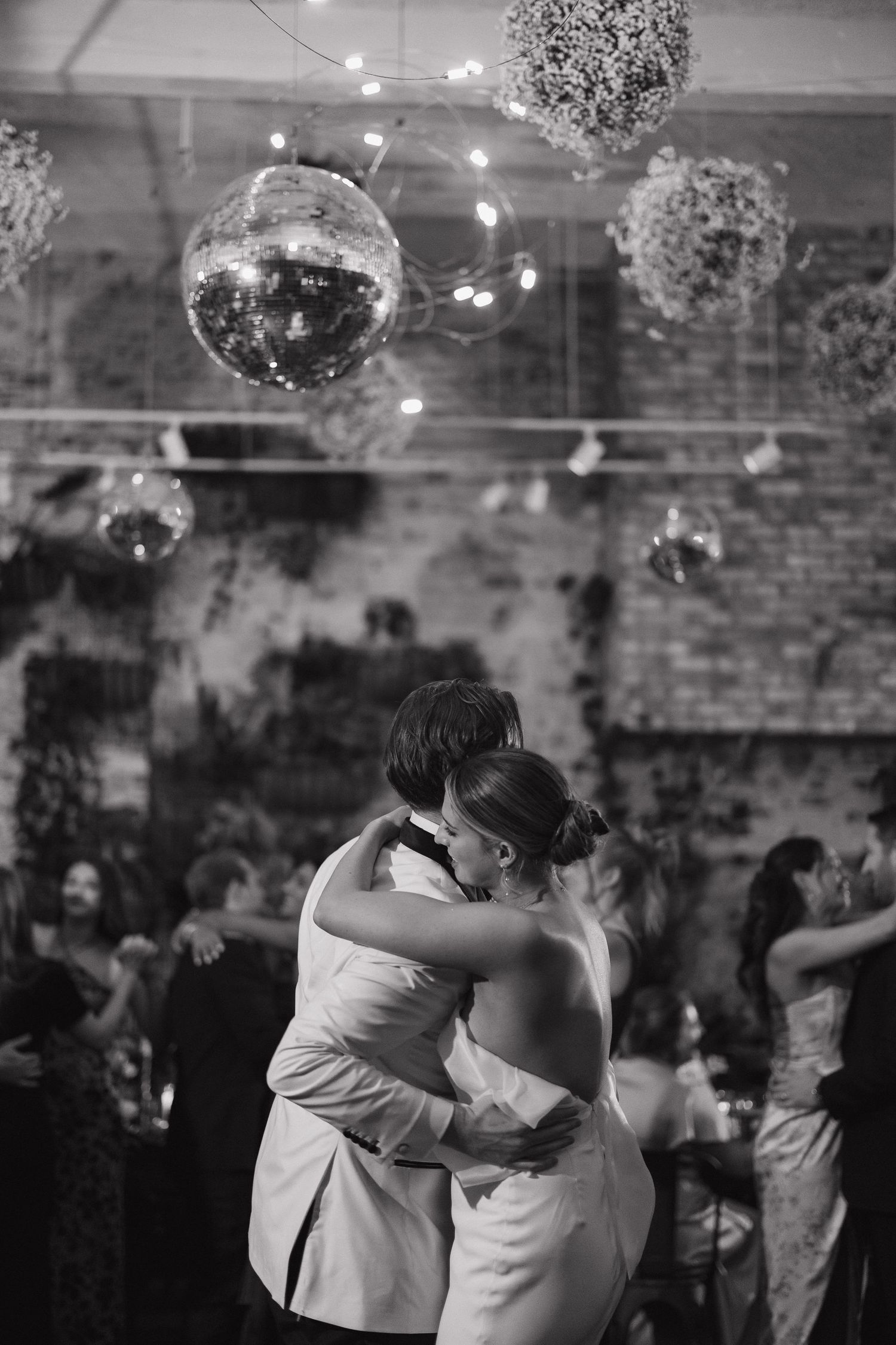 Black and white photo captures romantic first dance under sparkling disco balls at wedding reception.