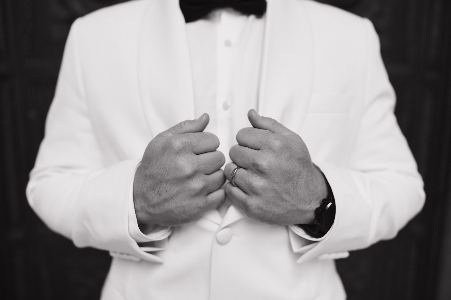 Close-up of hands adjusting a white tuxedo jacket against a dark background.