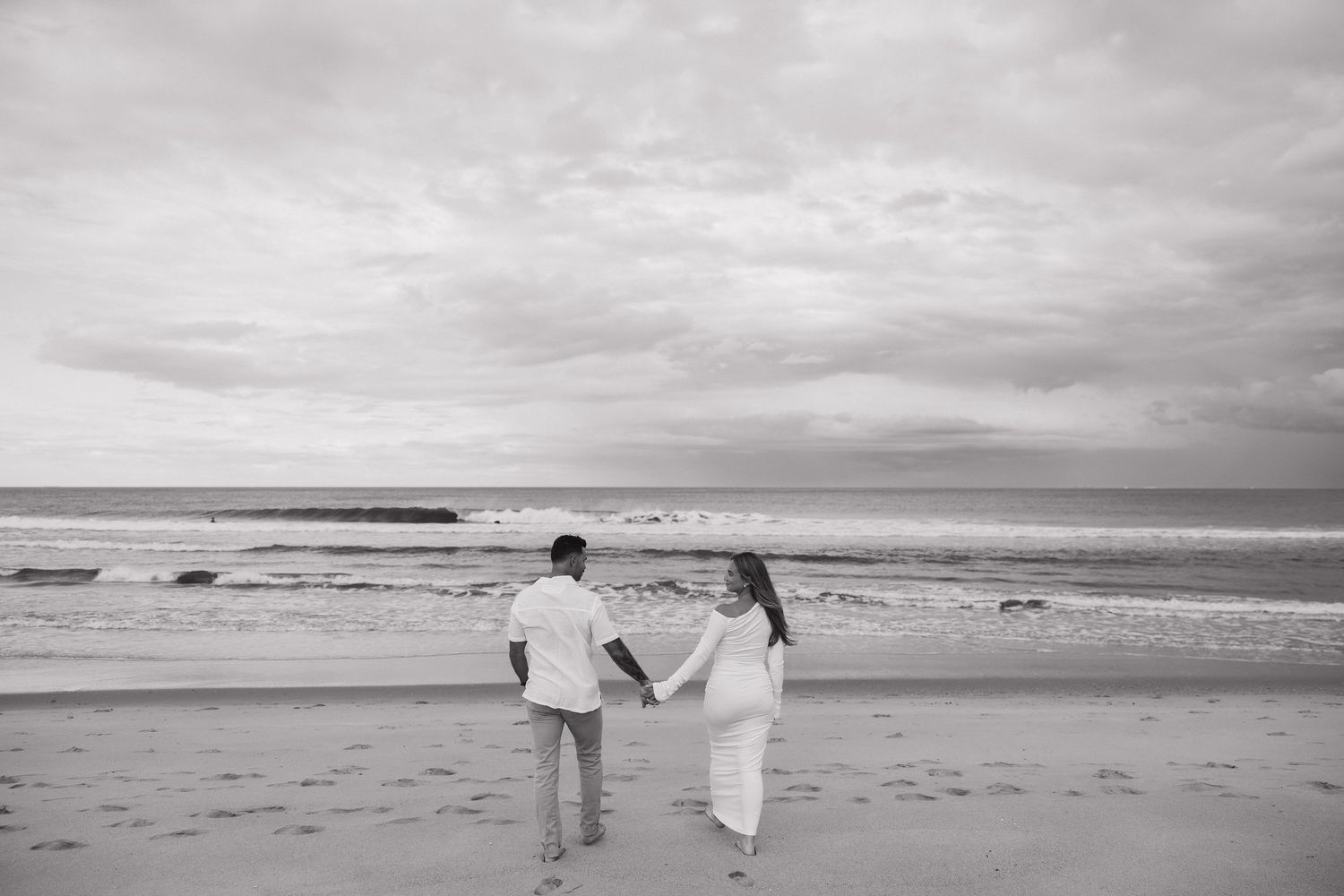 Two people walking along a misty beach shoreline at sunset.