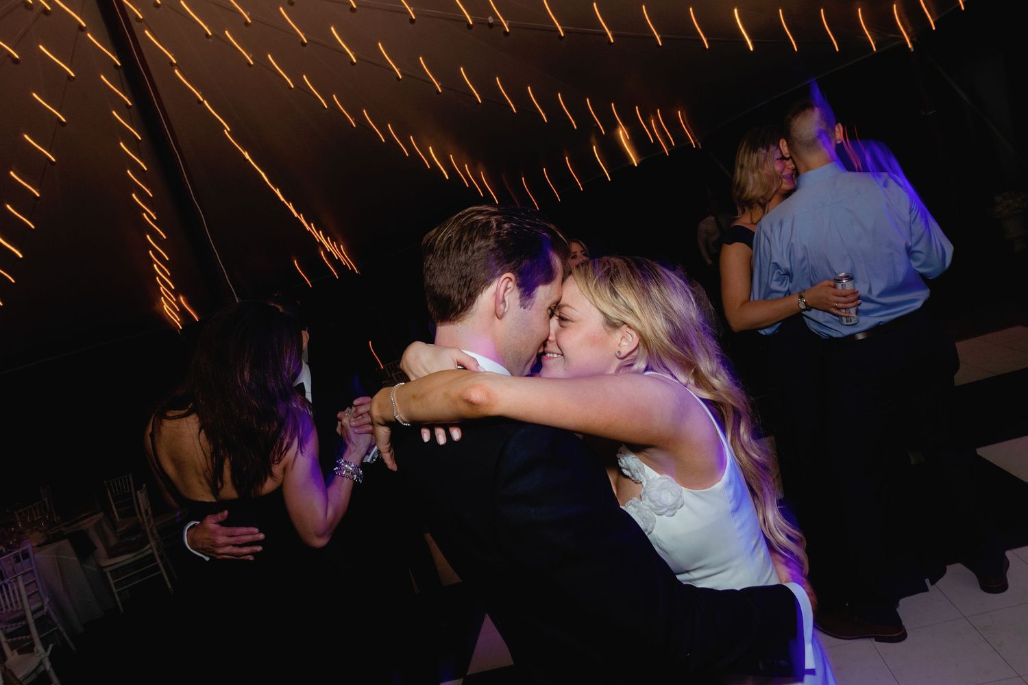 Couples dance under string lights at an evening outdoor wedding reception.