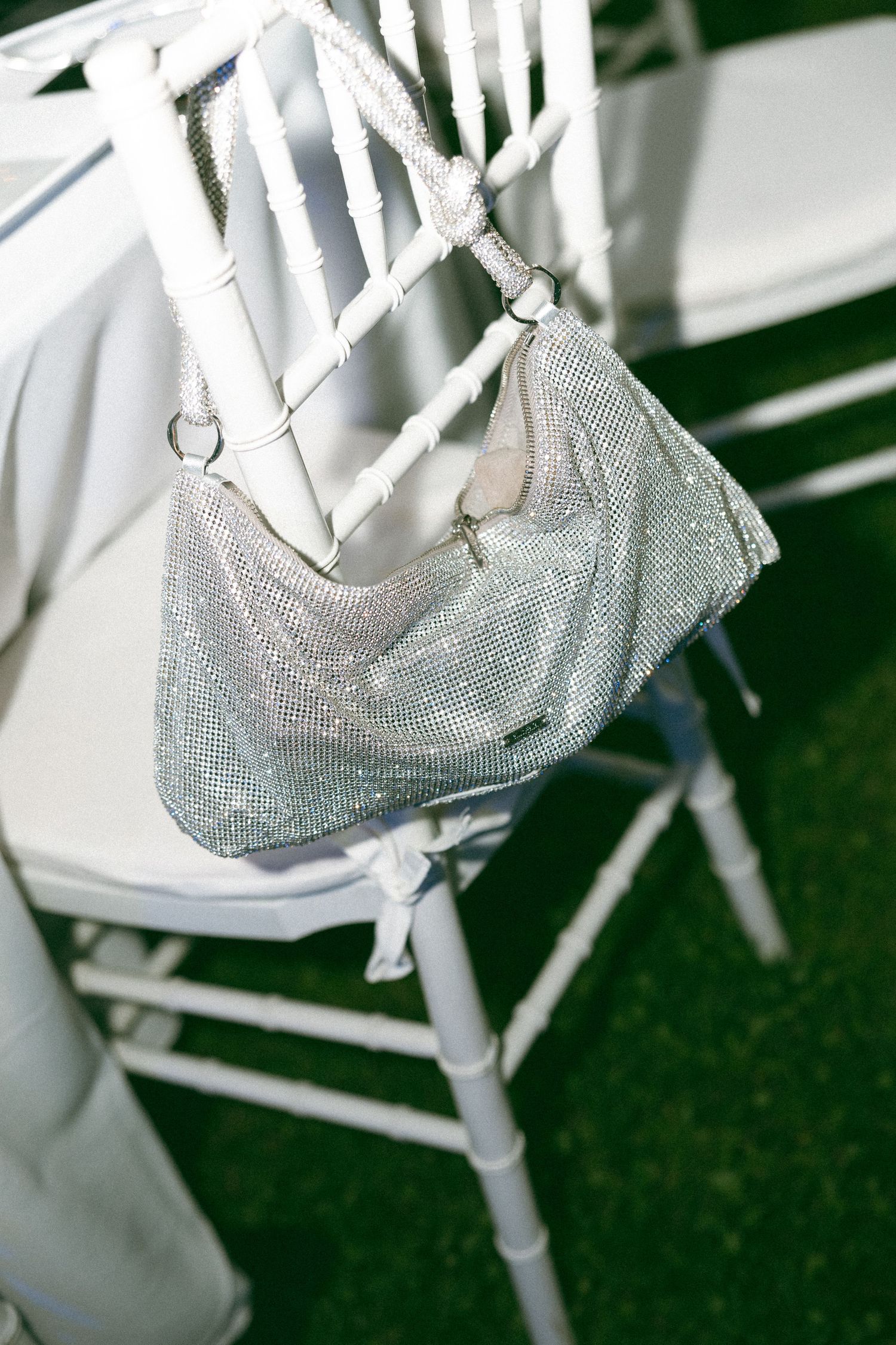 A sparkly silver evening bag hangs decoratively on the back of a white wooden folding chair.