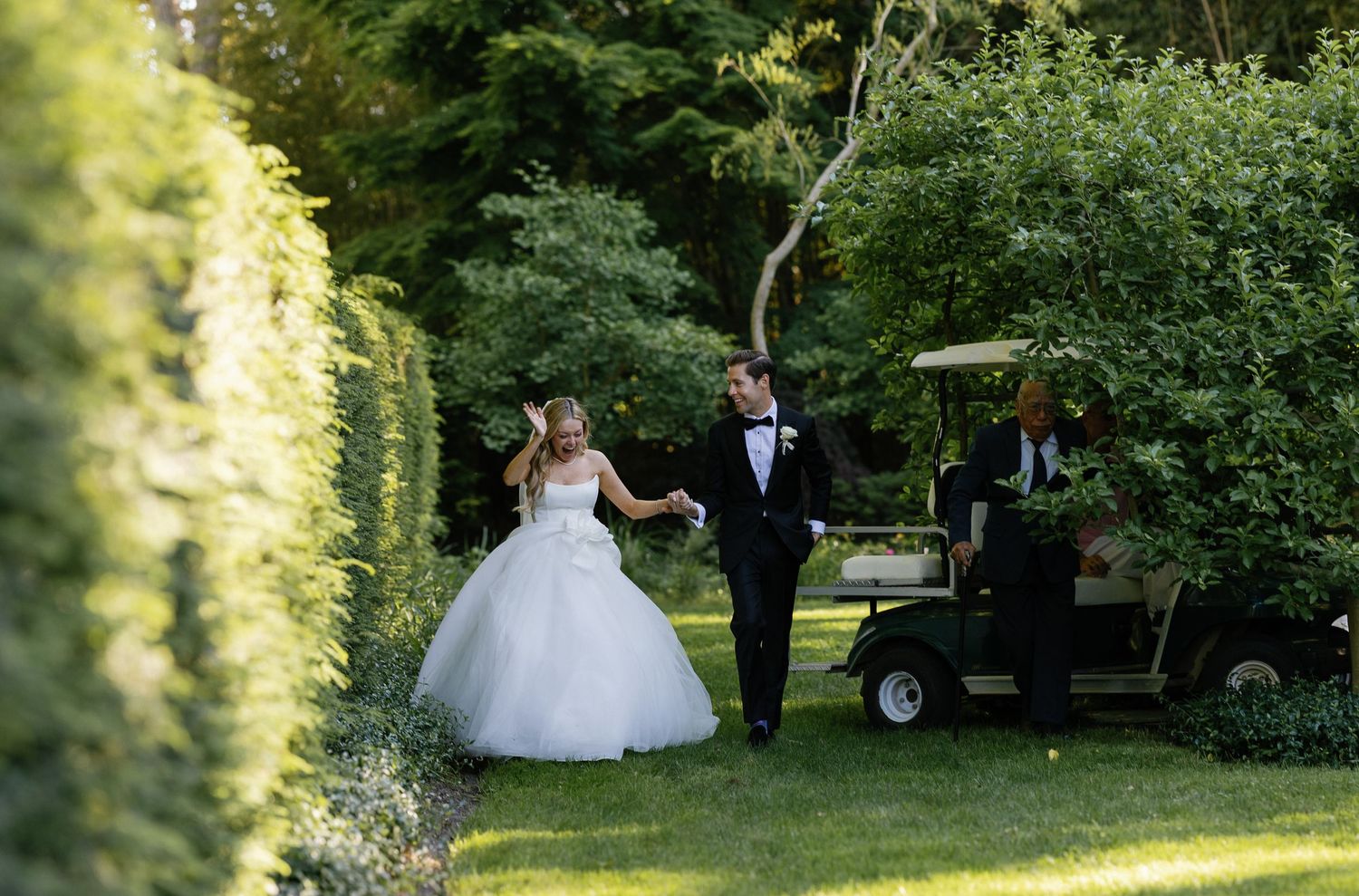 Wedding party walks through a lush garden path on a sunny afternoon.