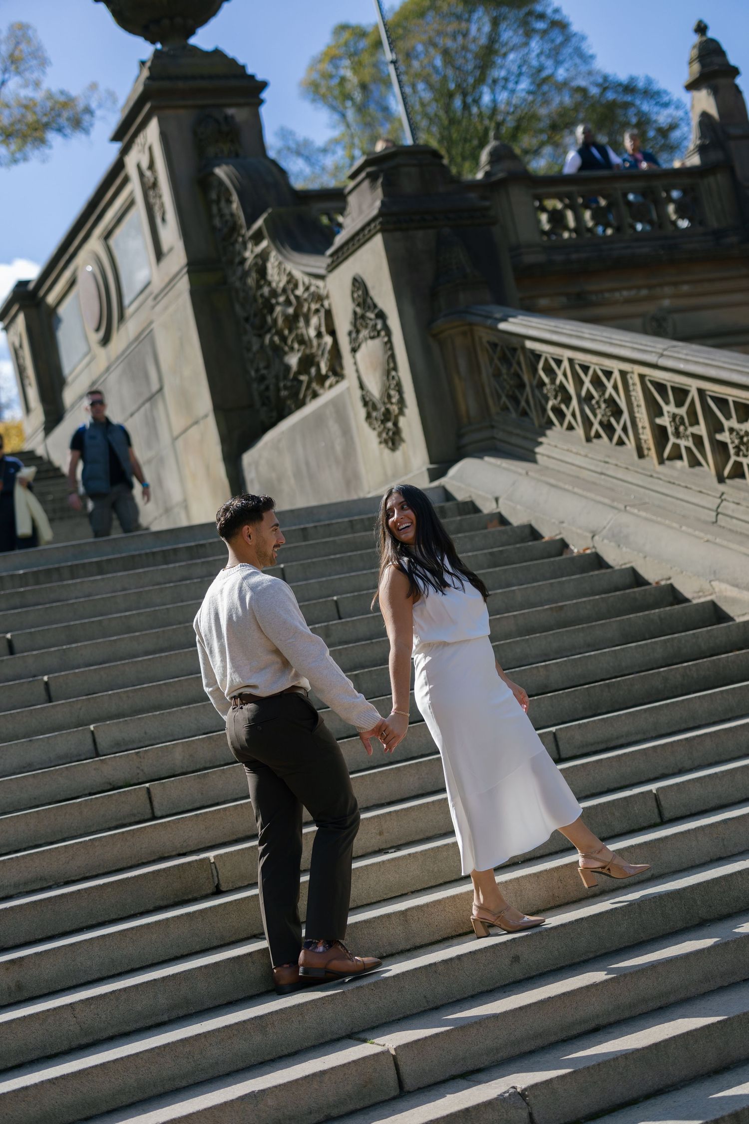 A couple in white outfits holding hands while ascending grand stone steps at a historic building.