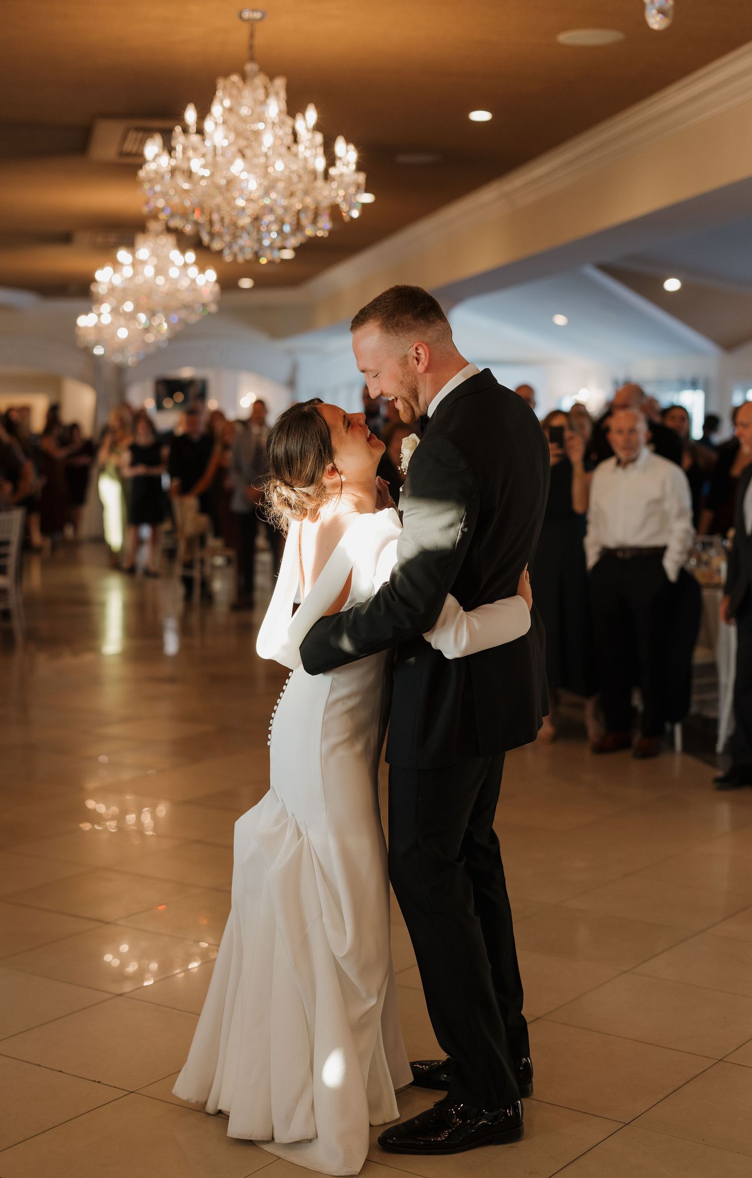 Wedding couple dancing under elegant crystal chandeliers in a spacious ballroom venue.