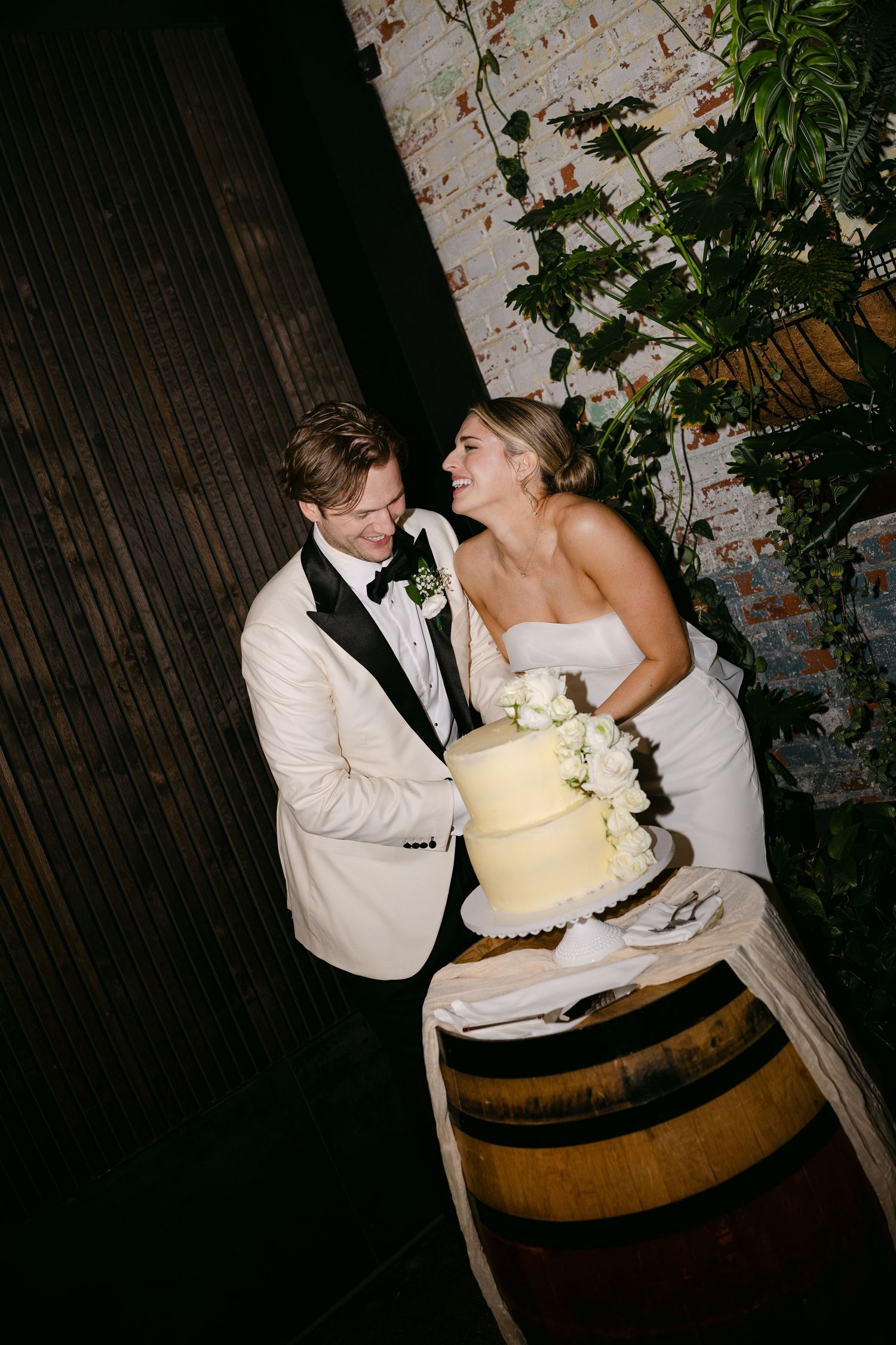 Couple shares intimate moment near rustic wine barrel during evening wedding reception.