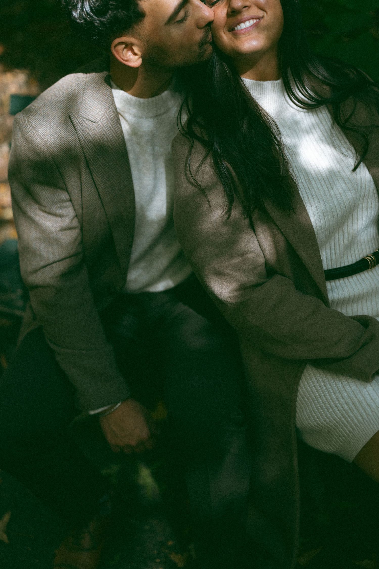 A couple in casual attire shares intimate moments in moody lighting outdoors.