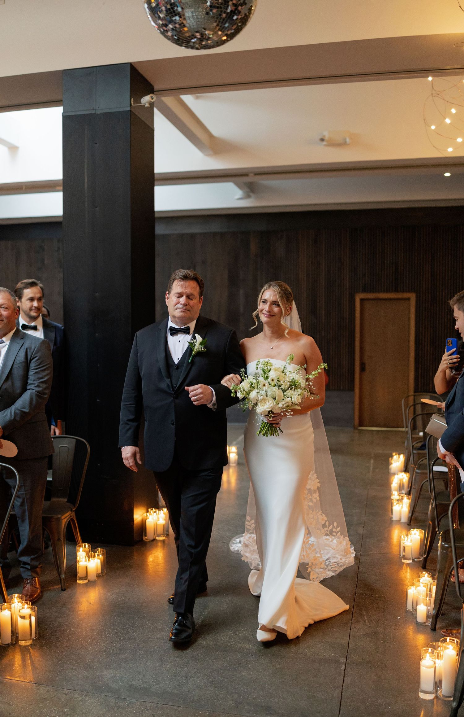A candlelit wedding ceremony aisle lined with glowing lanterns creates a romantic ambiance.