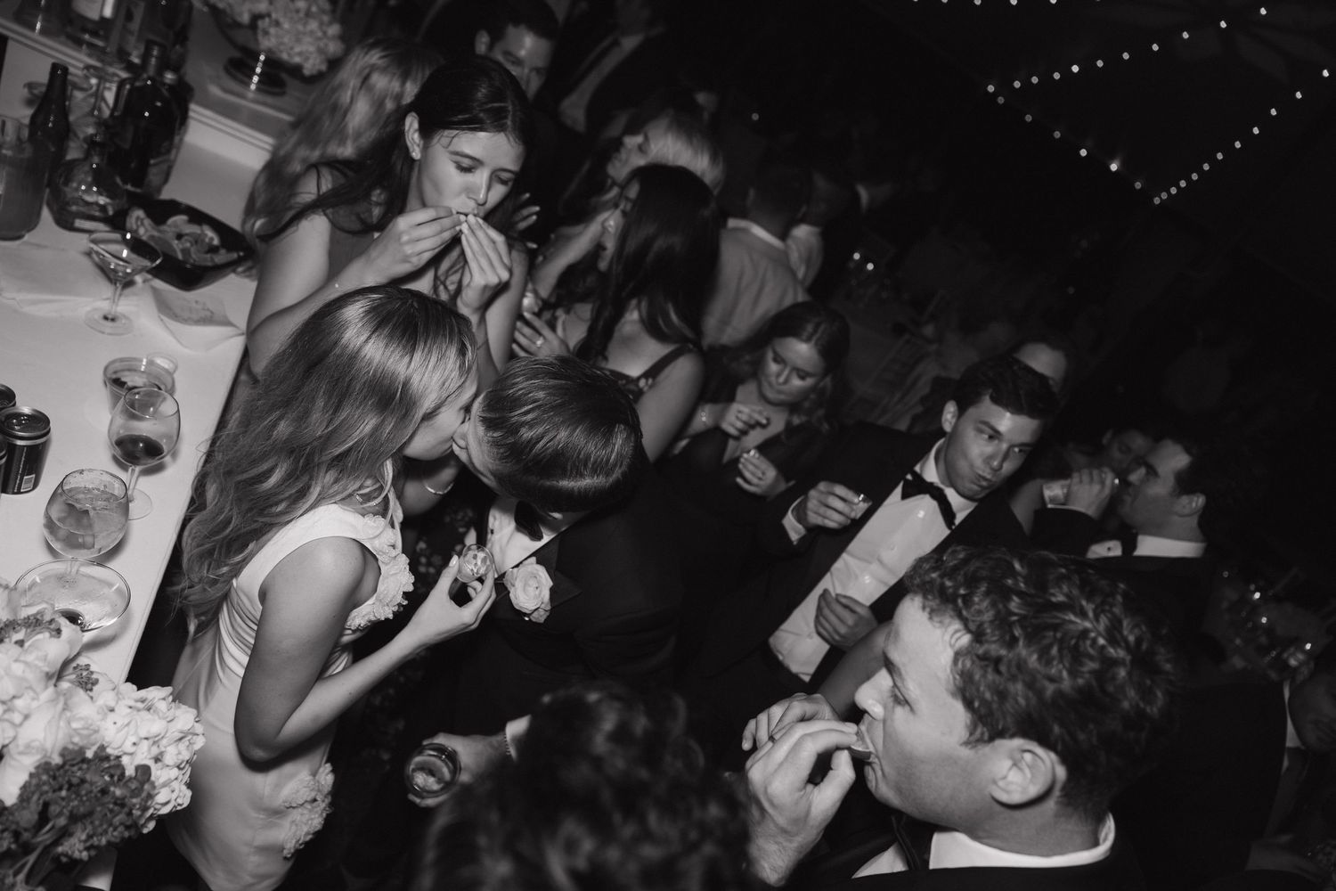 Dark reception venue illuminated by string lights as wedding guests dance.