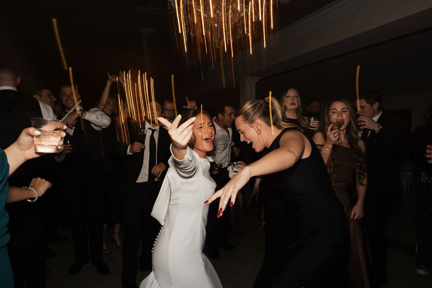 Dark reception hall with gold metallic streamers hanging from ceiling as party guests dance and celebrate.