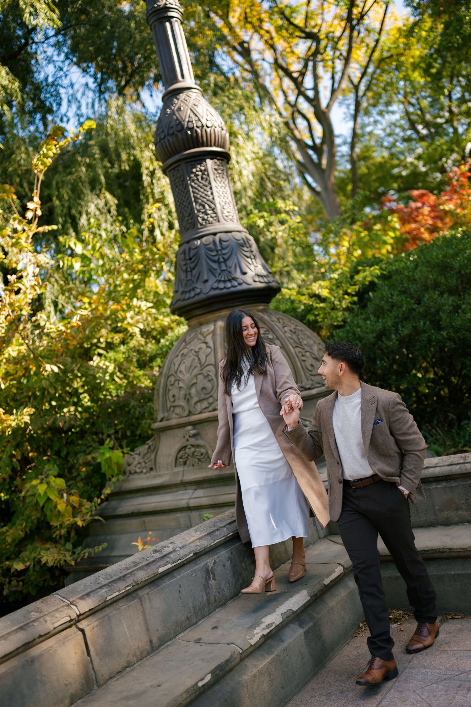 Couple sharing intimate moments on stone steps with ornate architectural details in a park setting.
