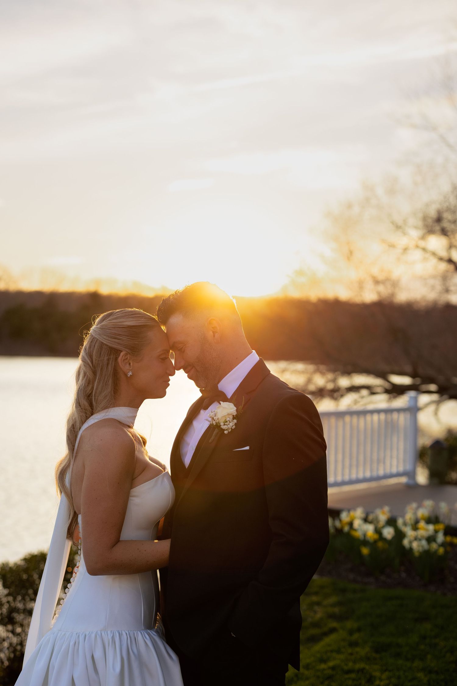 Bride and groom sharing a romantic sunset moment by a lakeside on their wedding day.