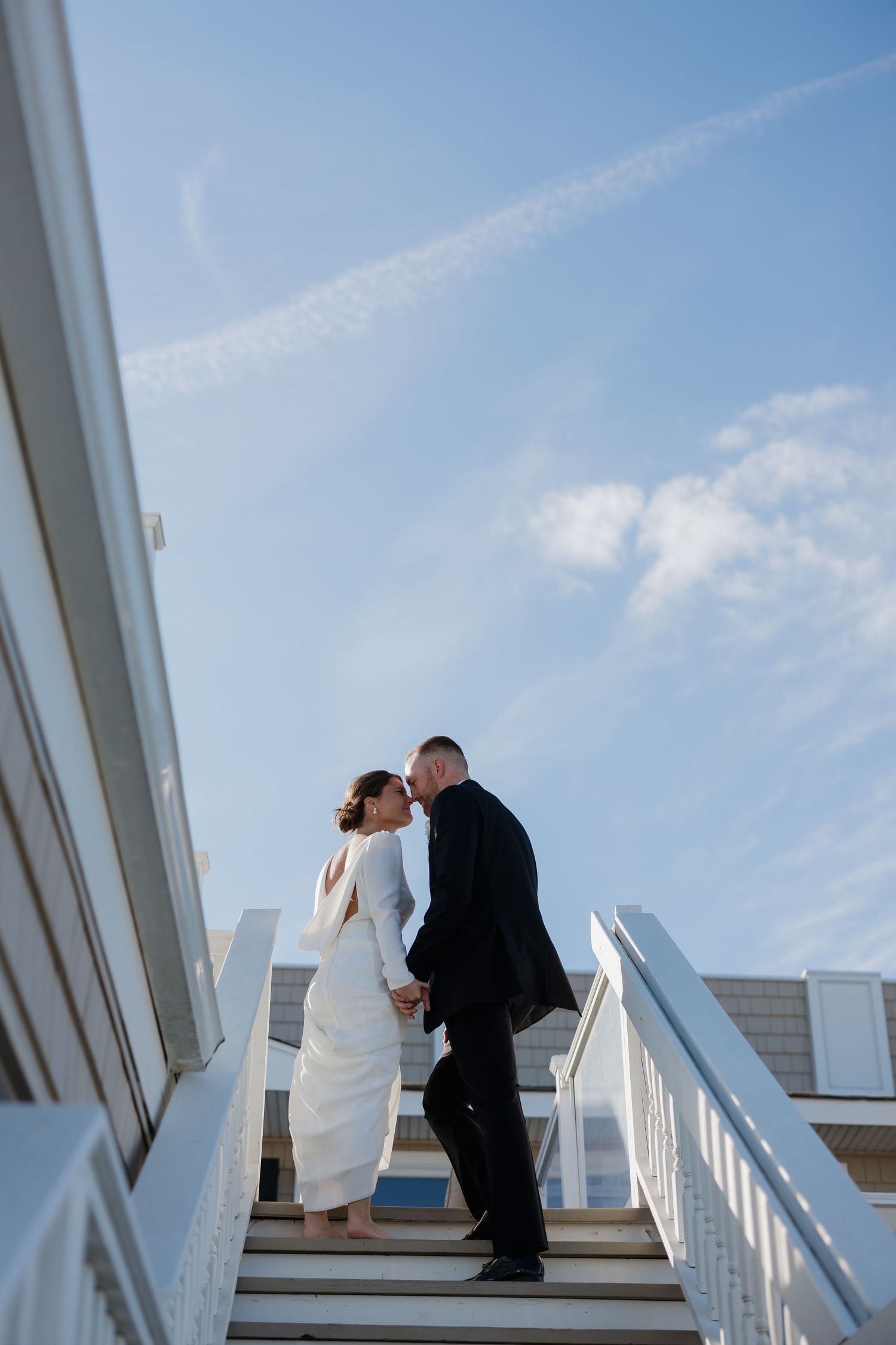 Couple shares romantic moment on white stairs against blue sky in artistic wedding photo sequence.