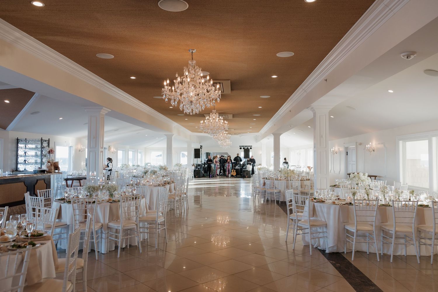 Elegant white wedding reception venue with crystal chandeliers and round tables set for a formal celebration.