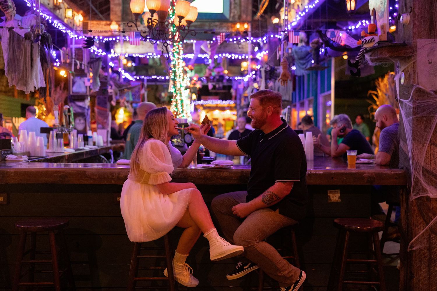 A dimly lit bar interior with purple neon lighting and patrons seated at the counter.